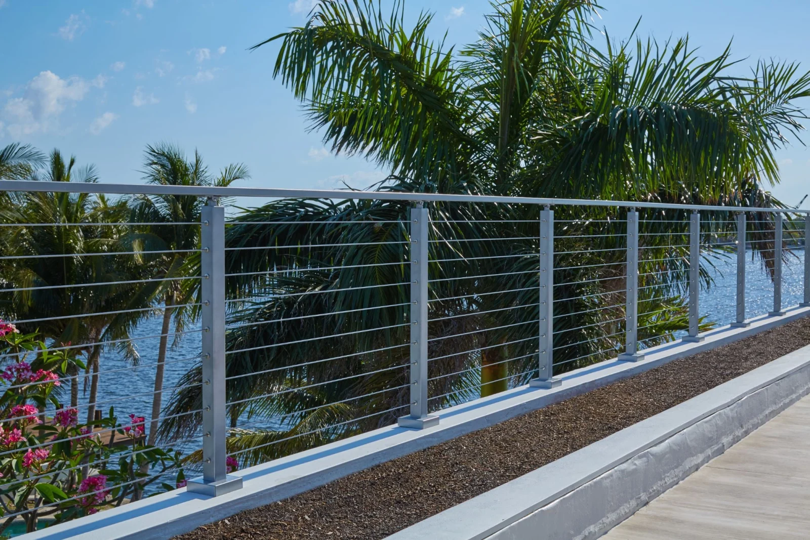 Railing running the length of a gravel-edged path lined with palm trees