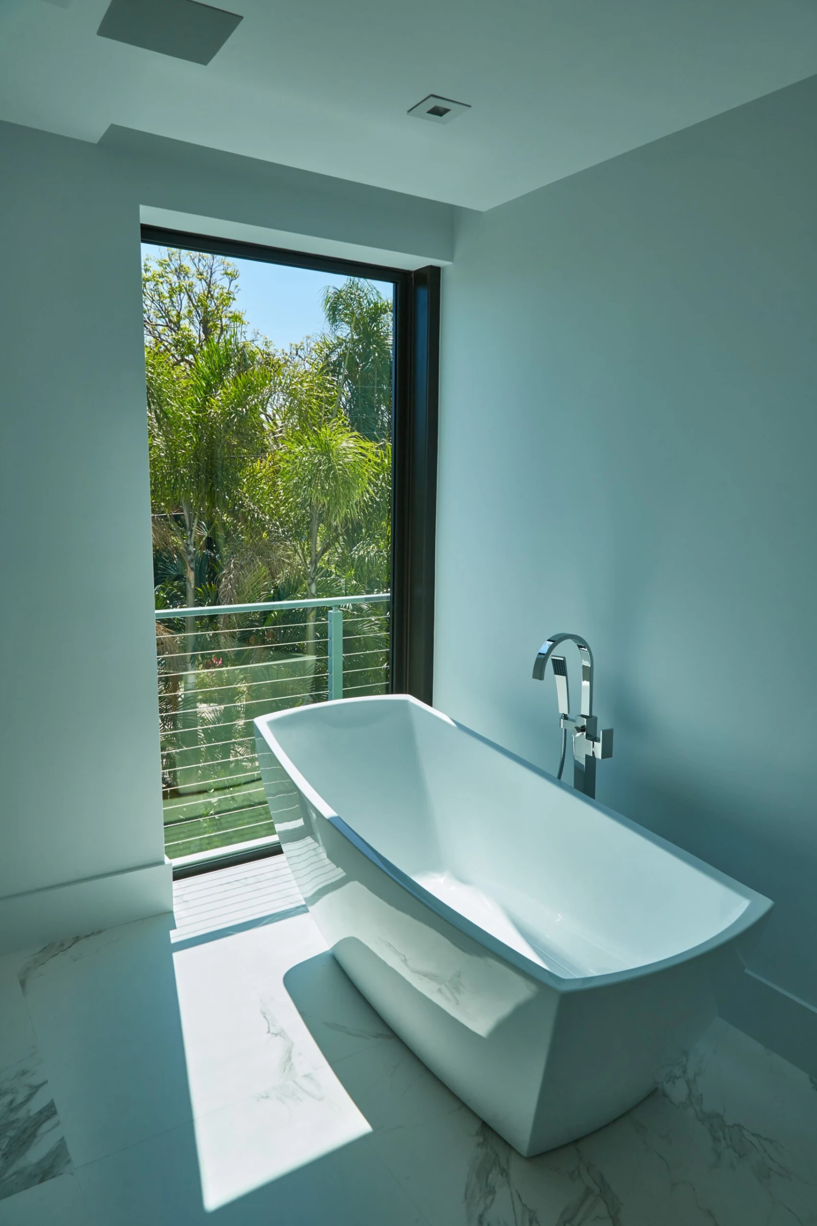 Bathroom looking out to a railed balcony framed by tropical greenery