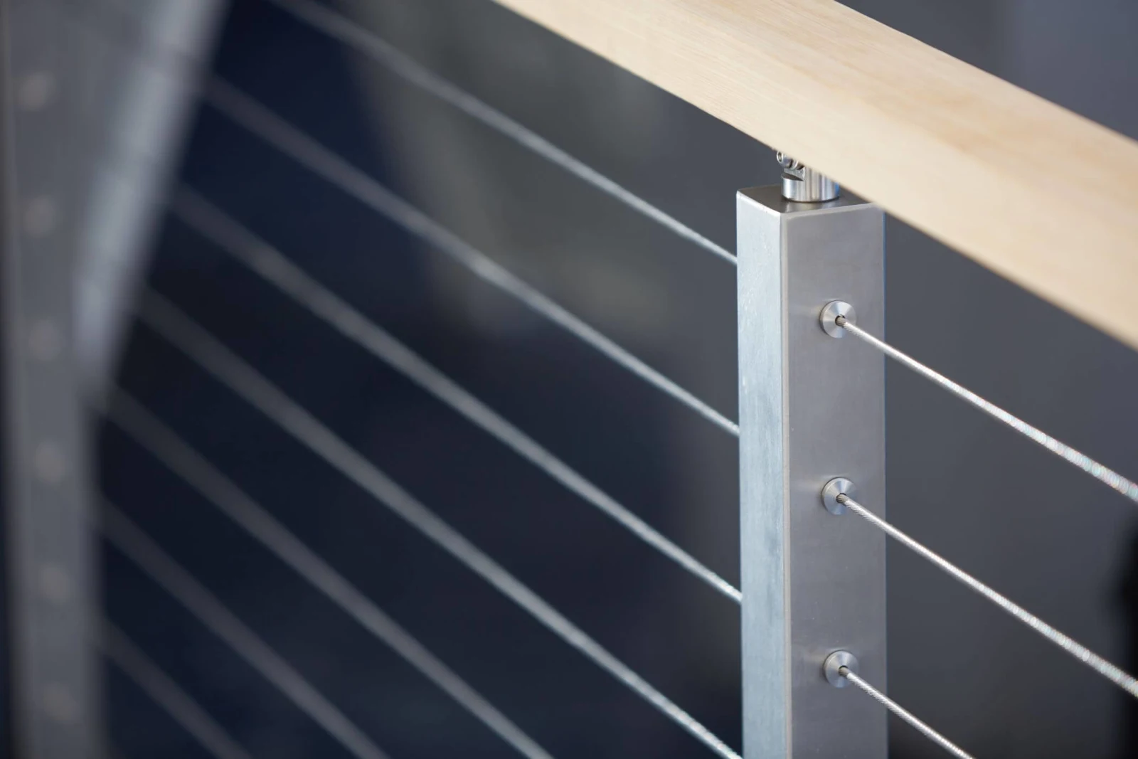 Close view of cable ends swaged into a stainless post below a wood rail
