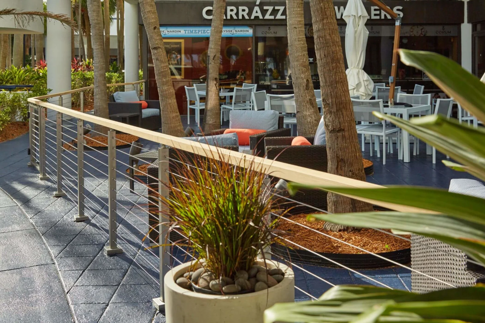 Wood-topped cable railing curving past planters at a courtyard cafe