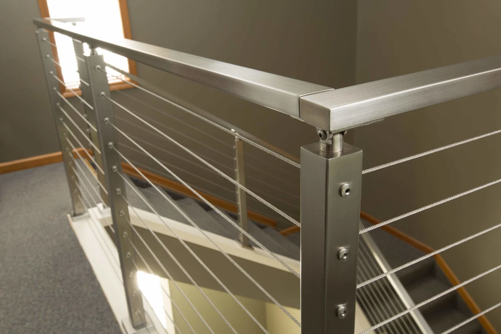 Stainless posts and a flat metal top rail meeting at a corner above an open stairwell