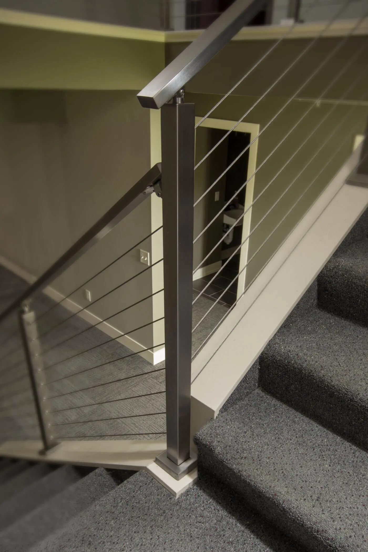 Stainless newel and cable infill at the foot of a carpeted stair