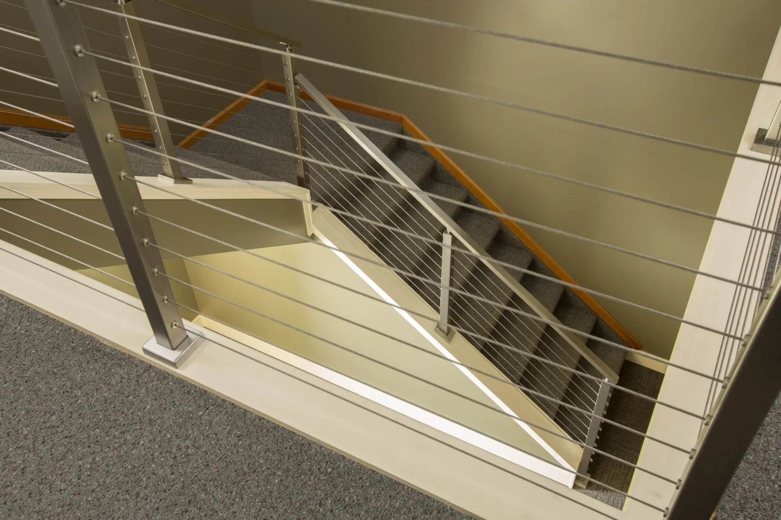Landing railing looking down a carpeted flight with cable infill