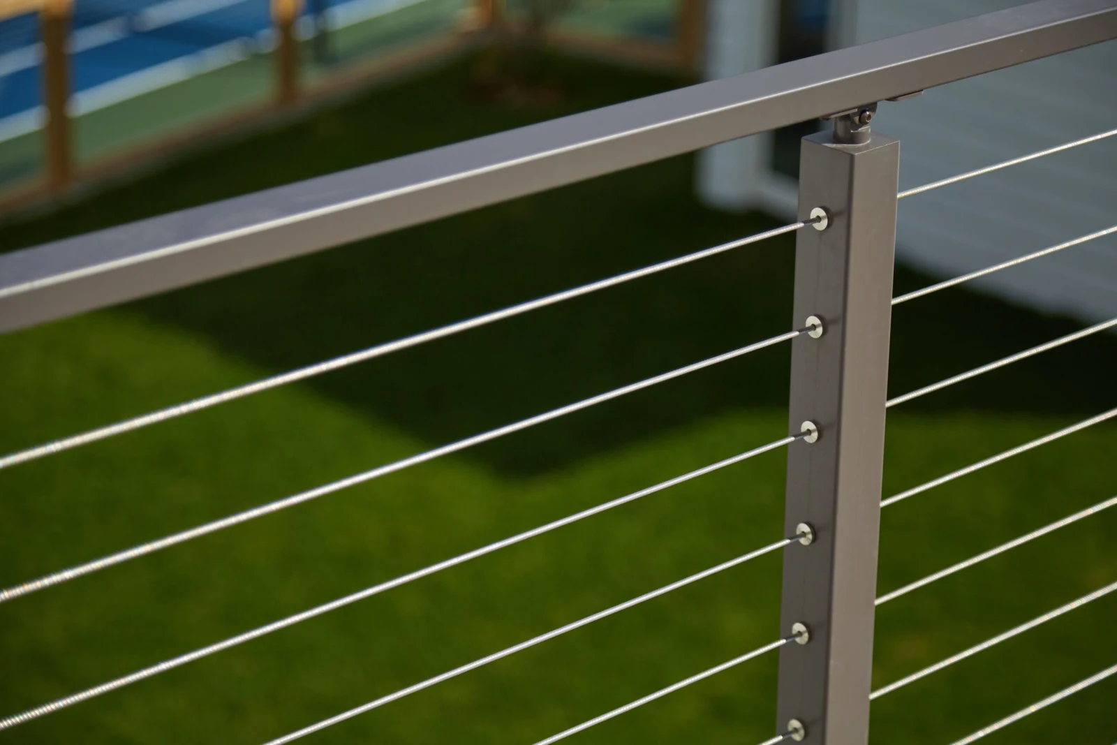 Close view of a gray post and cable run above a turf lawn
