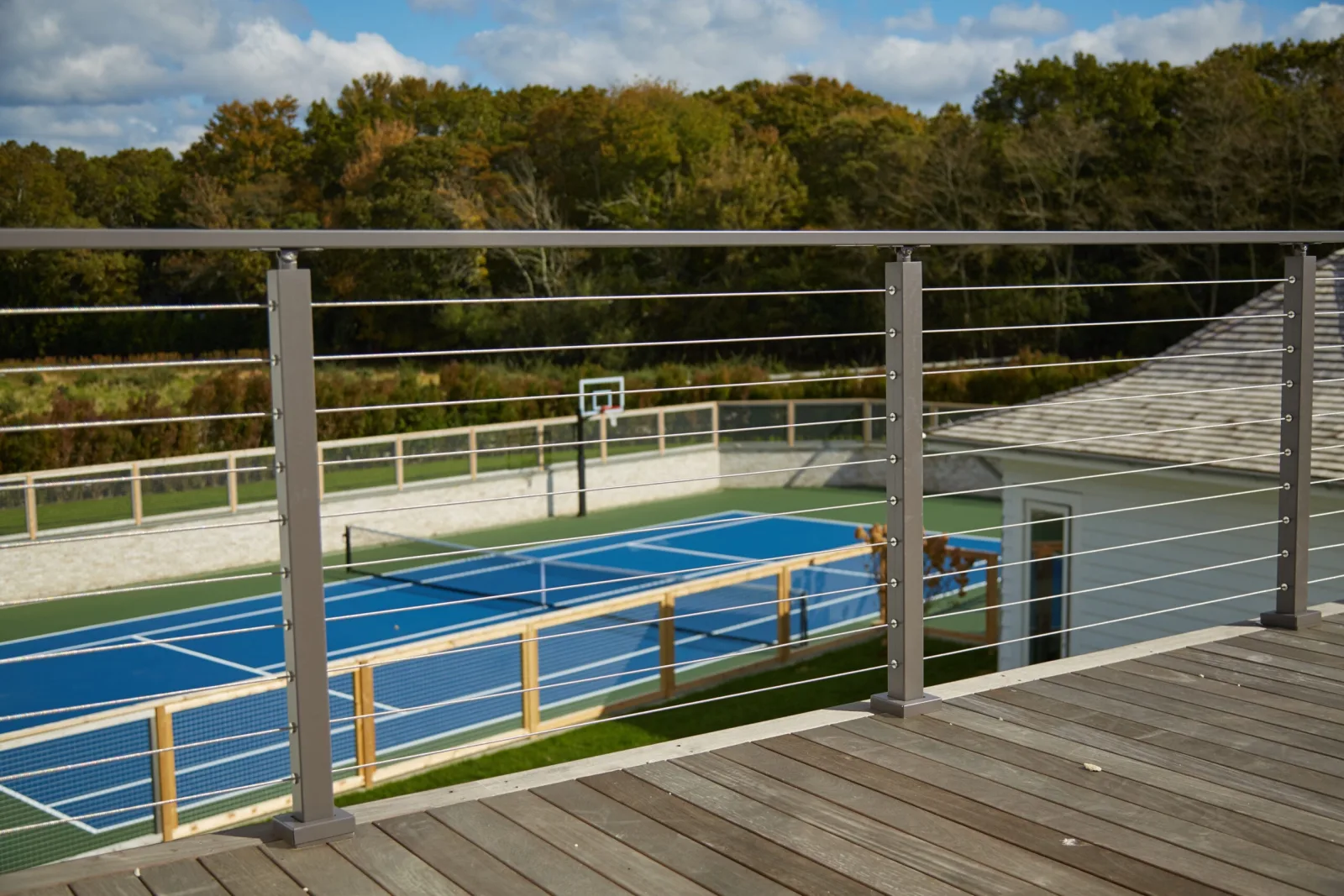 Silver cable railing along a plank deck looking out over a blue sport court