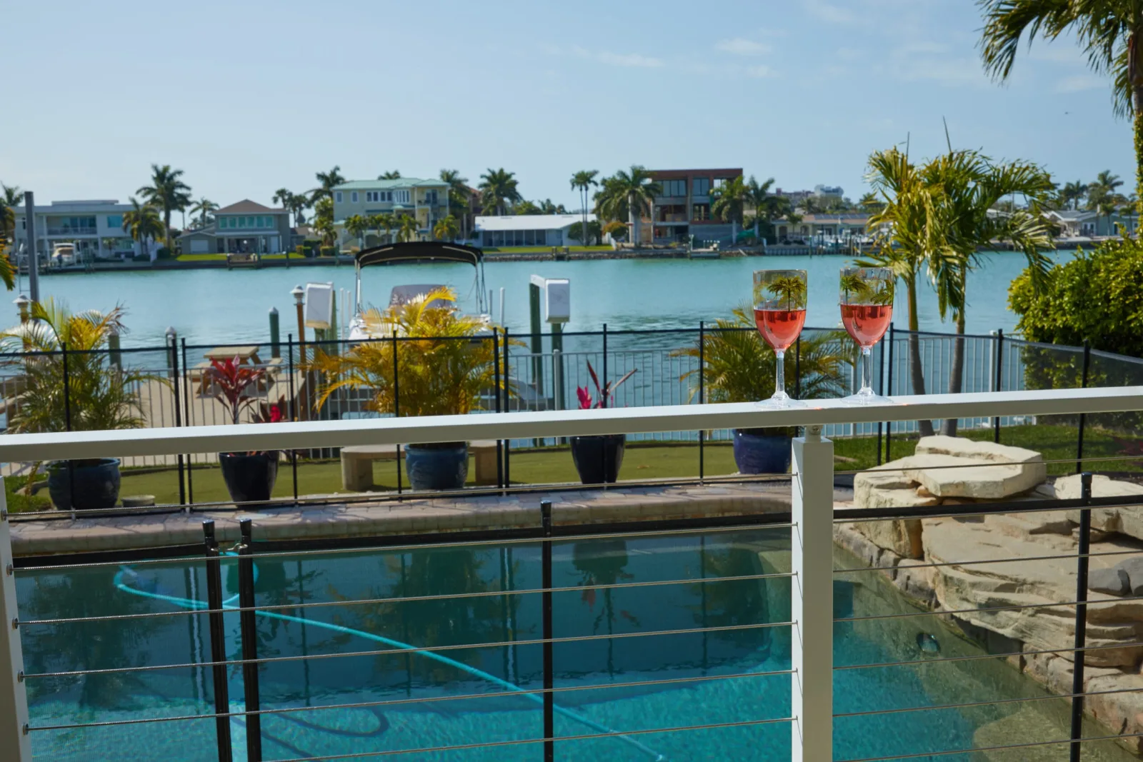 Two wine glasses on a wide white top rail above a pool and canal