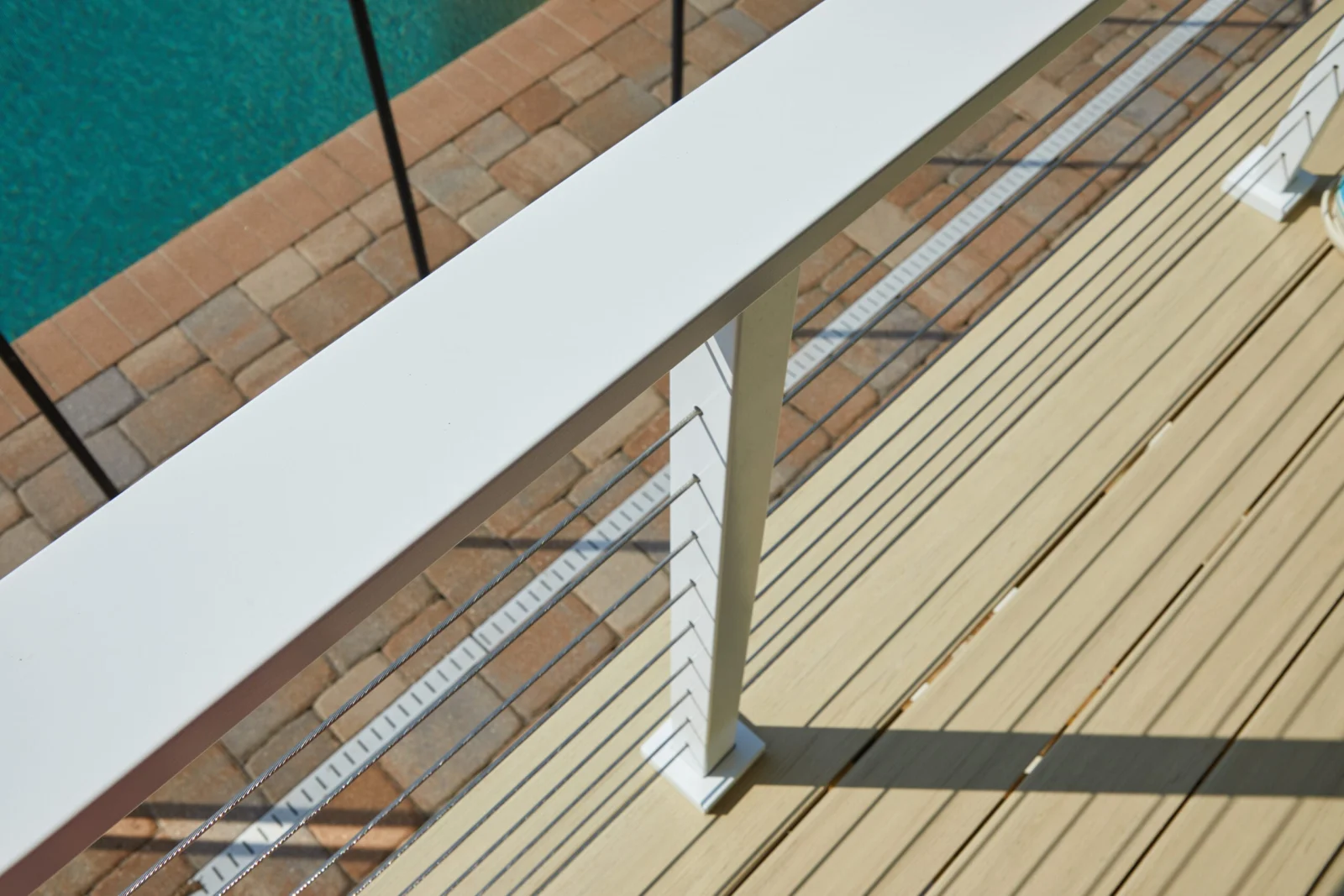 Wide flat white top rail angled above a poolside deck and brick pavers