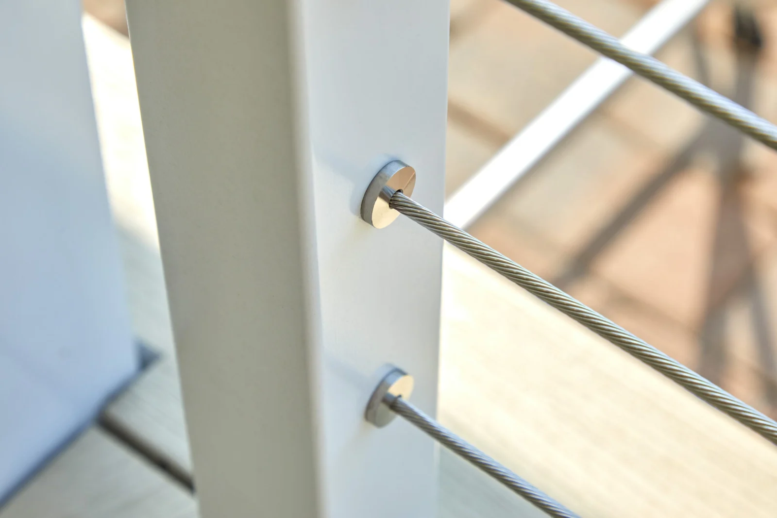 Cable end fittings anchored through a white powder-coated post, close view