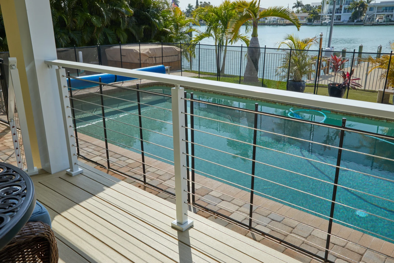 White cable railing along a pool deck with waterfront and palm trees beyond