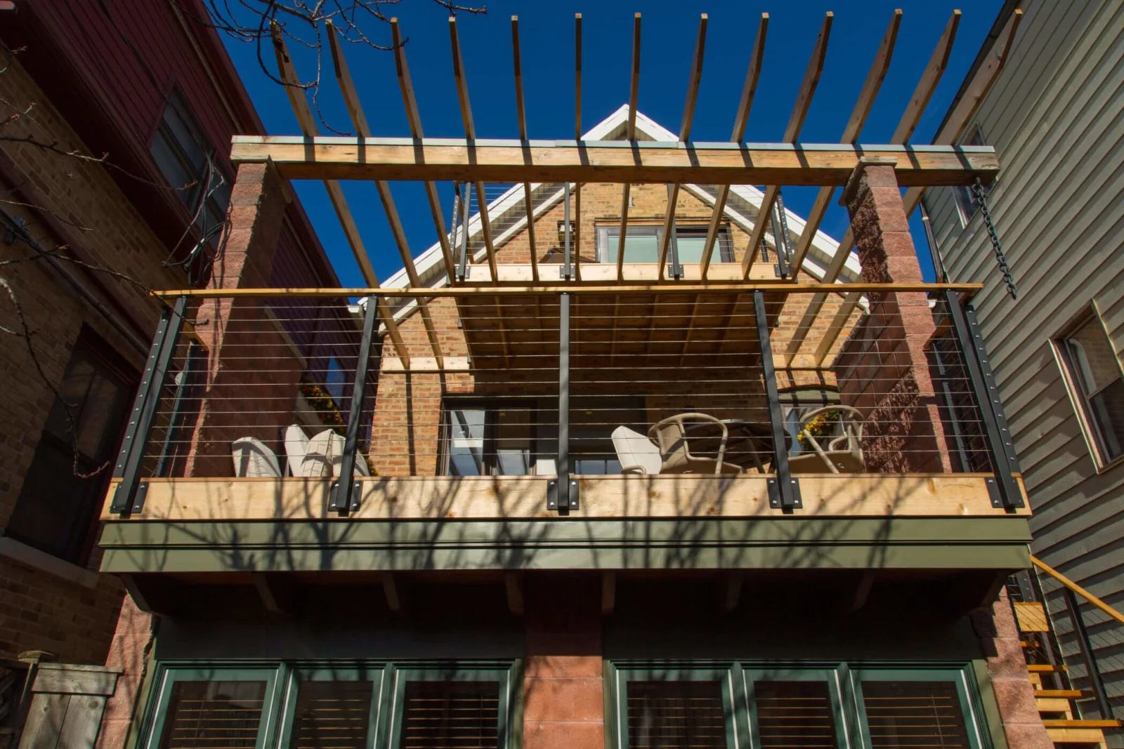 Straight-on view of a pergola-covered deck edged in cable railing above green shutters