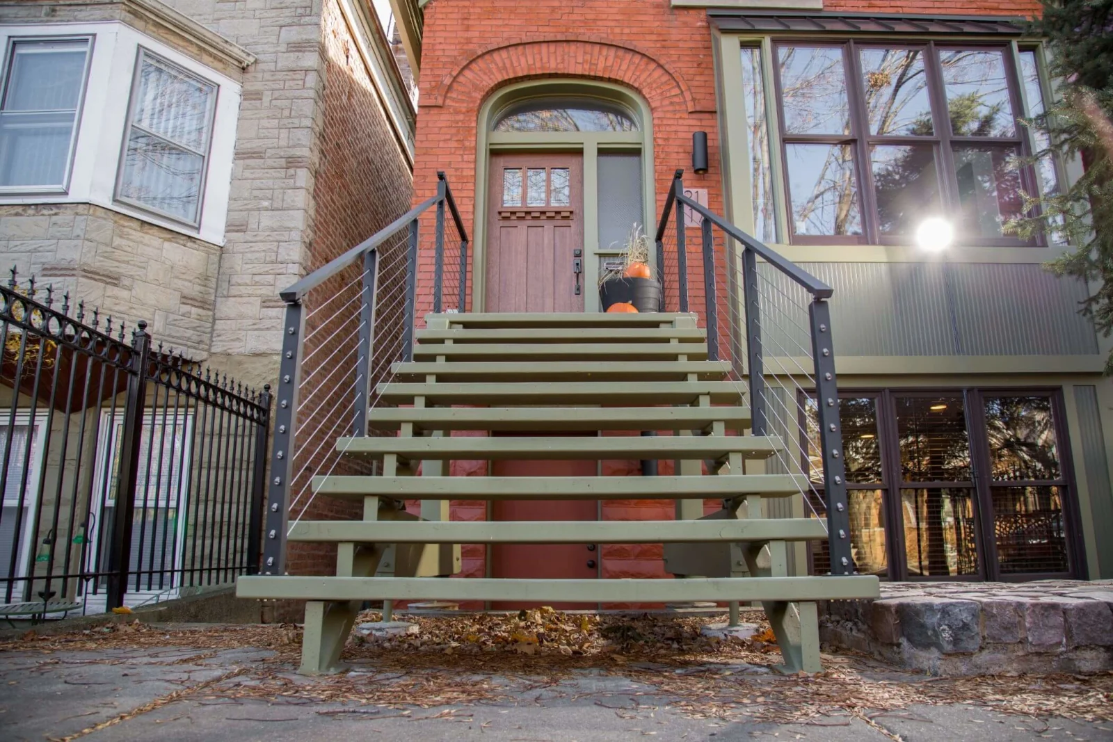 Painted wood steps with black cable railing leading to an arched brick rowhouse entry