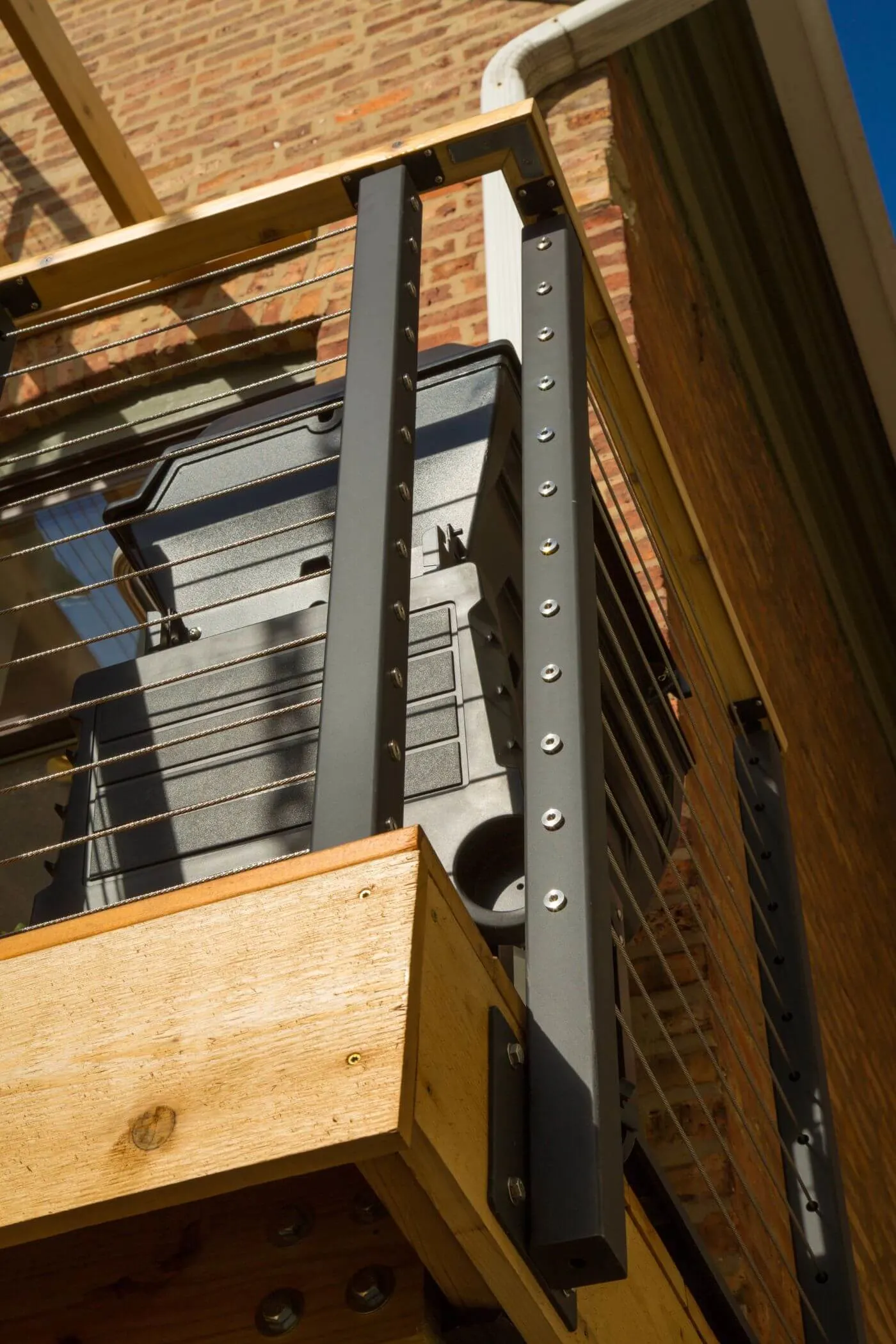 Upward view of a dark post and cable runs against a brick wall