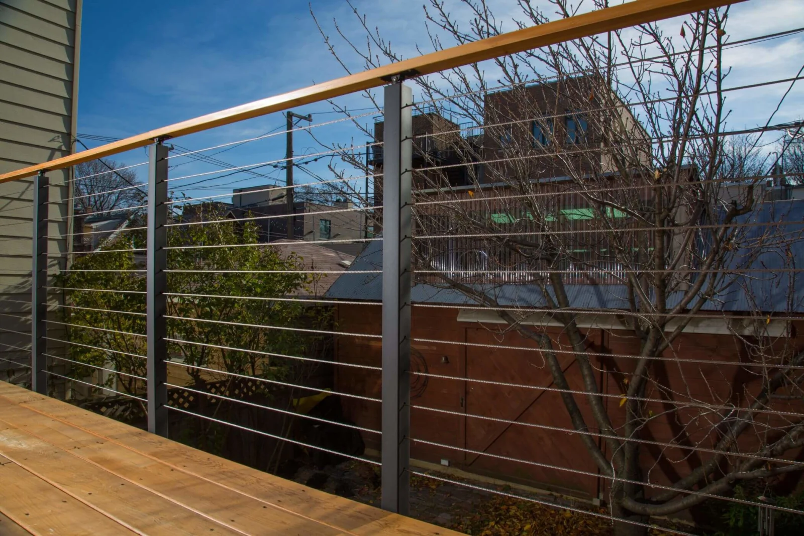 Deck-level run of cable railing with rooftops and bare trees behind