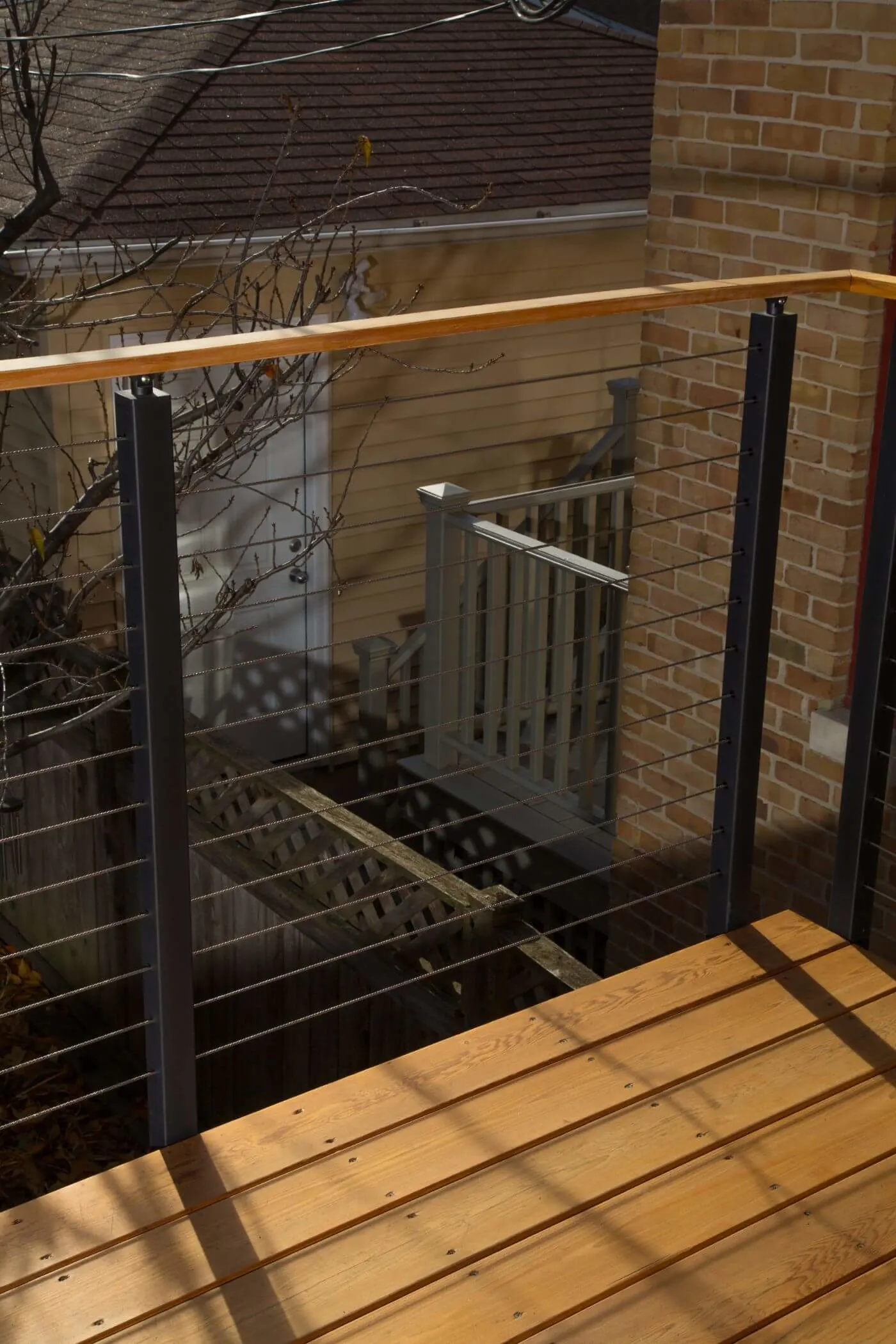 Corner of a wood deck where cables meet a warm wood top rail