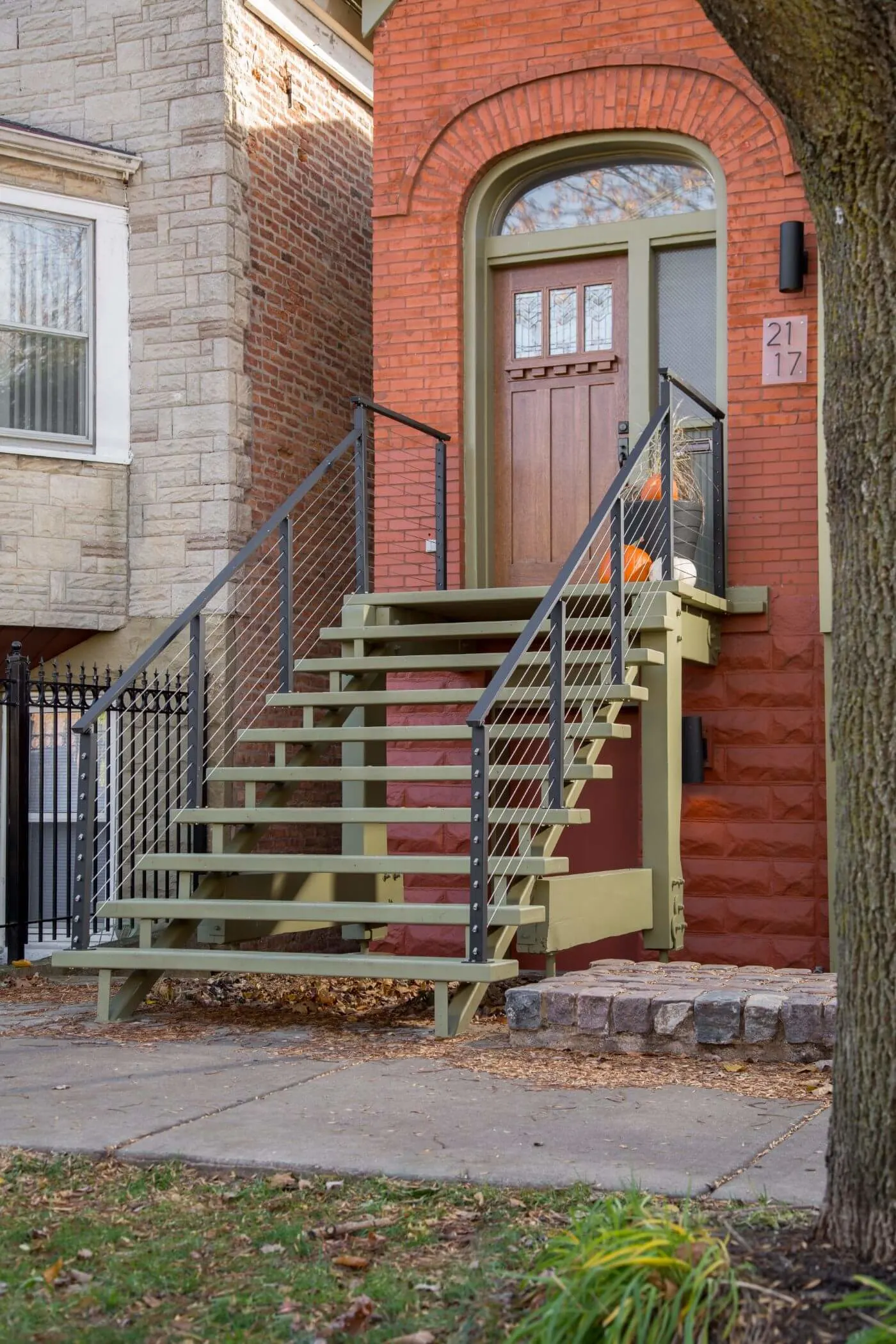 Street view of a brick rowhouse stoop with dark posts and cables