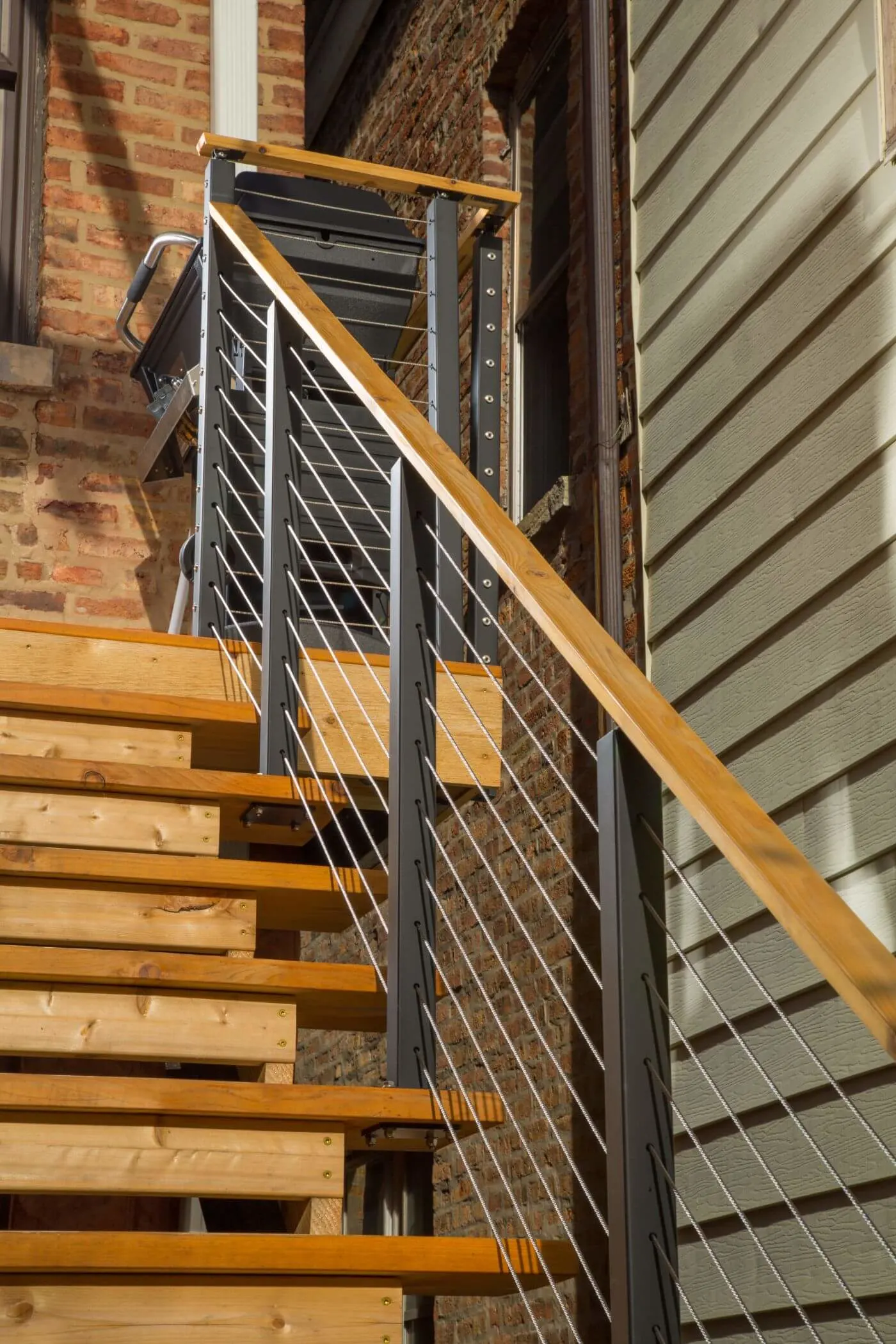 Open-riser wood stair with cable railing running between siding and brick