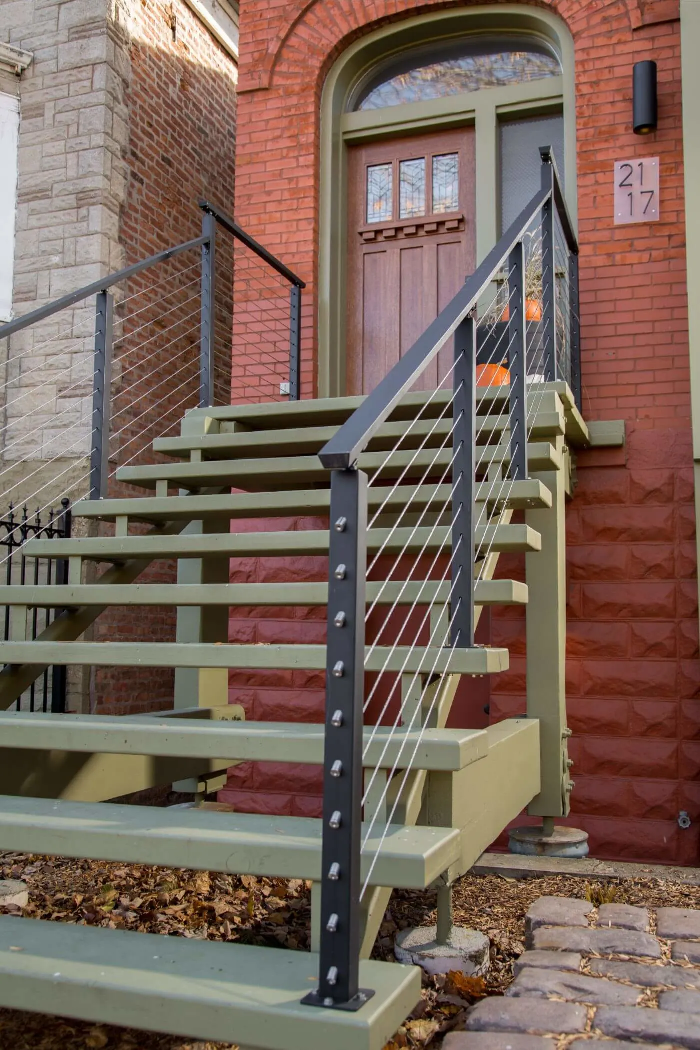 Front stoop stairs with dark cable railing beneath an arched brick entry