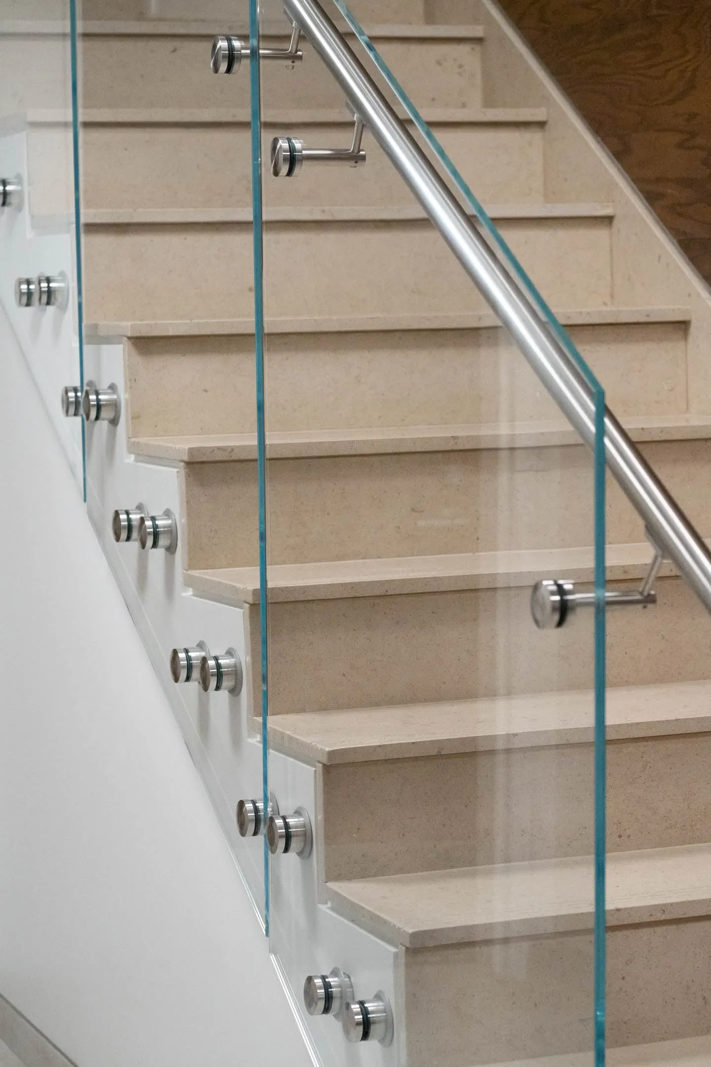 Glass panels on point fixings beside pale stone treads and a round handrail