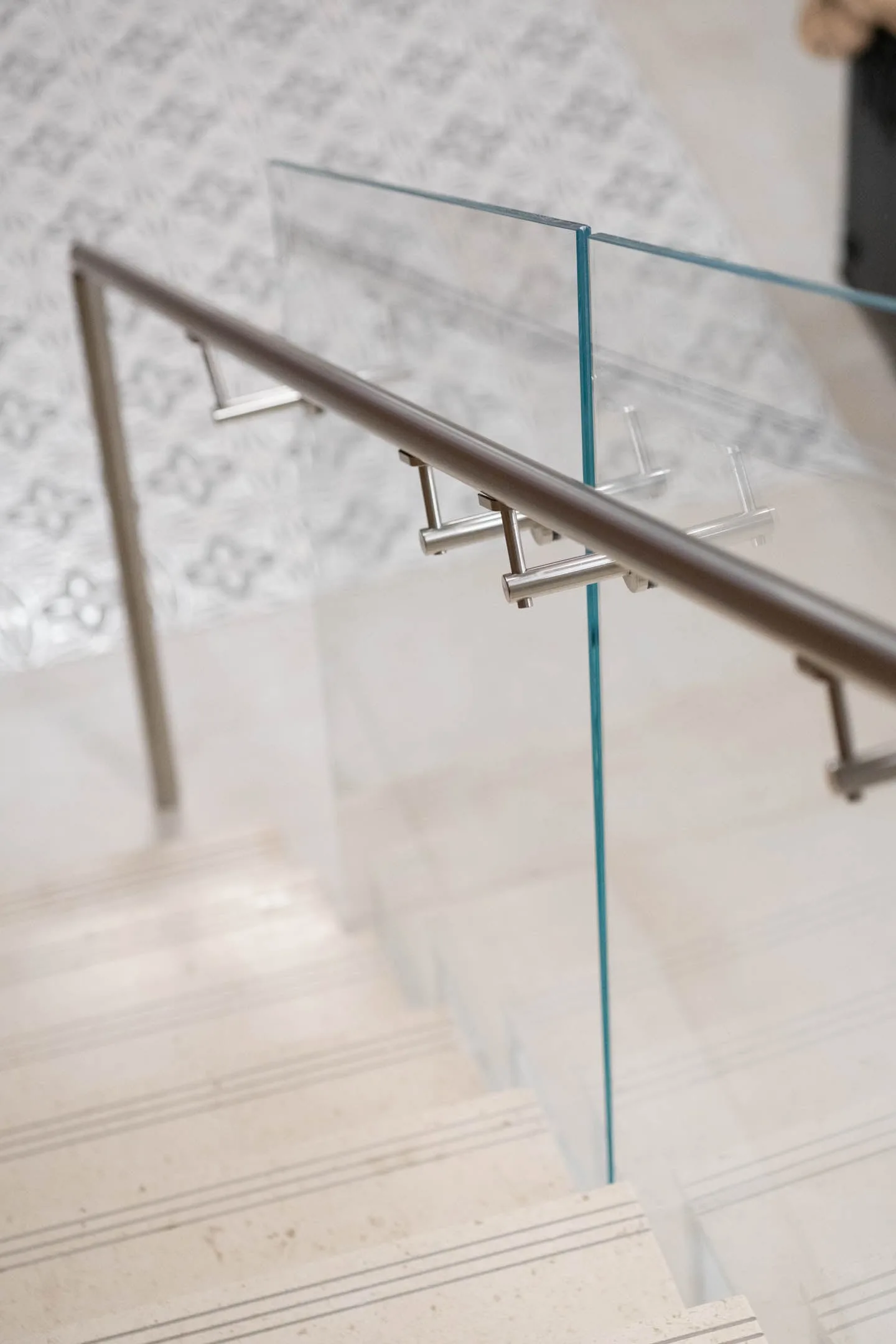 Downward view of a stainless handrail crossing glass above patterned tile