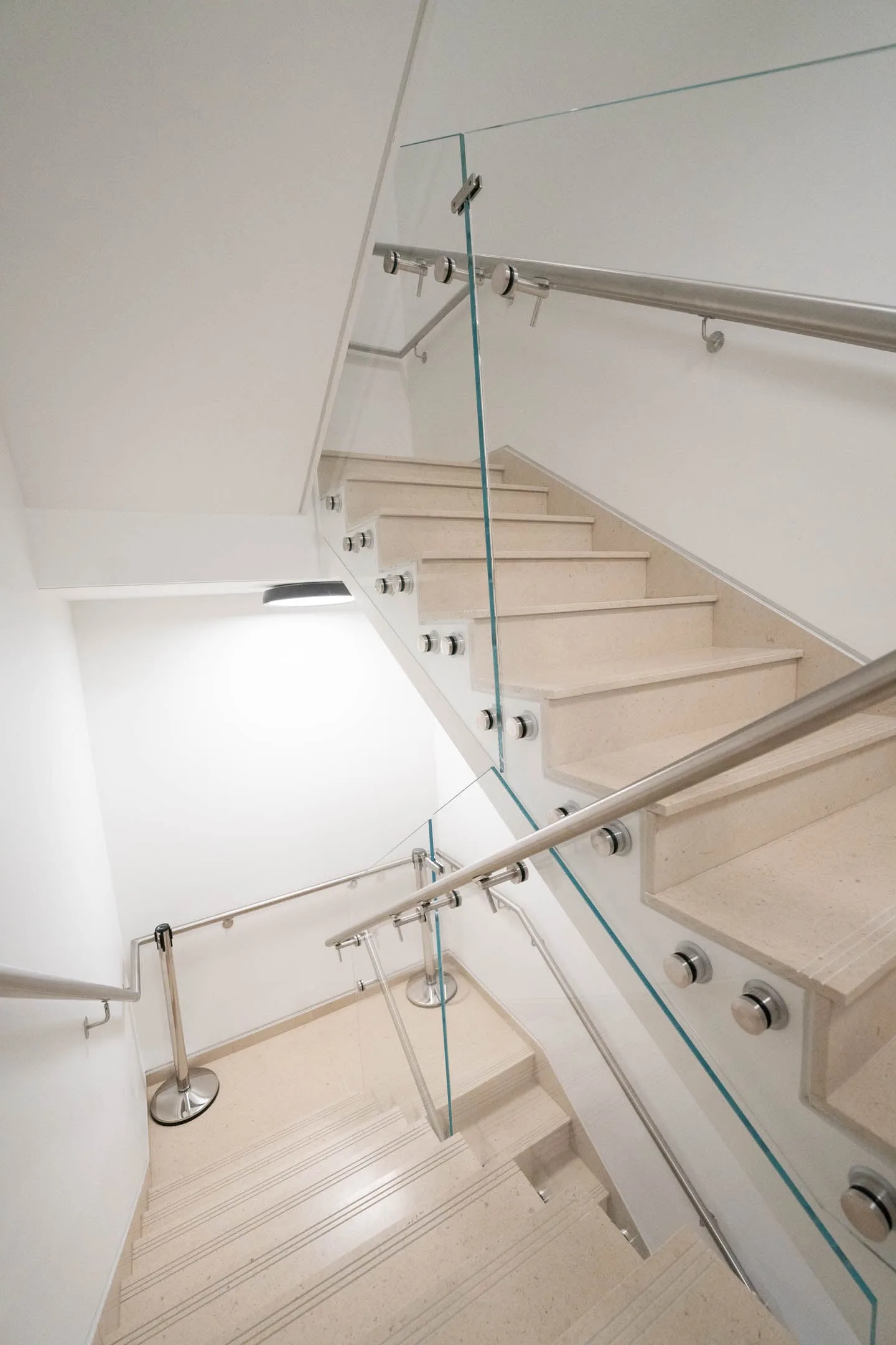 Overhead view down a switchback stair with glass railing on both flights
