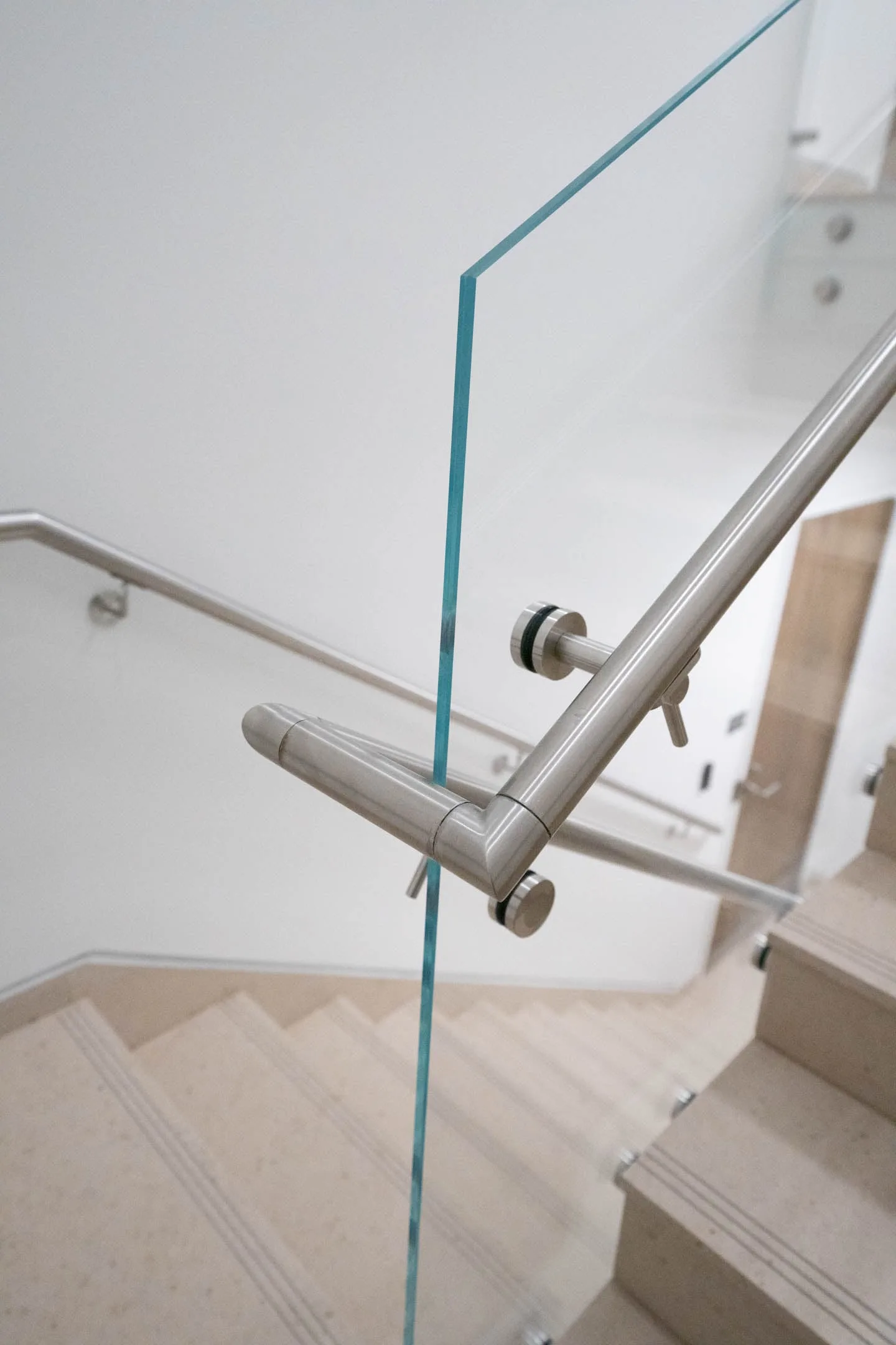 Round stainless handrail turning at a landing where it clamps through glass