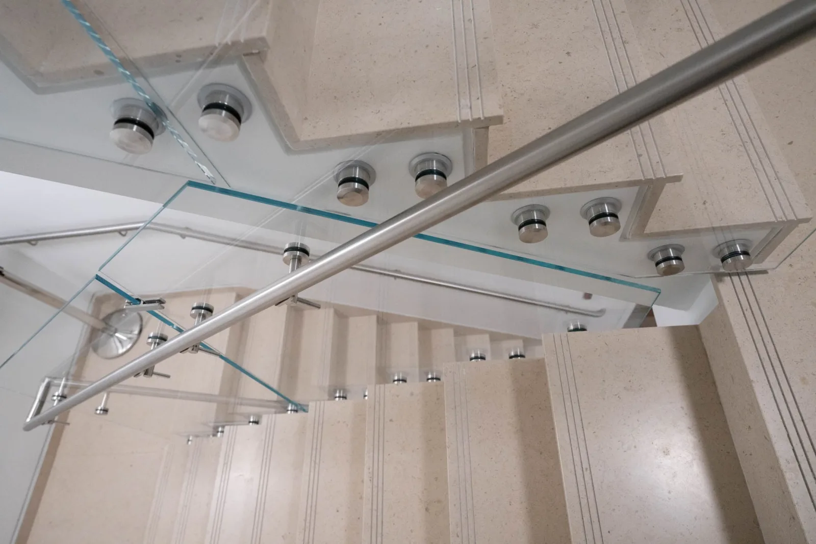 Upward view of glass railing, standoffs and handrail against stone treads