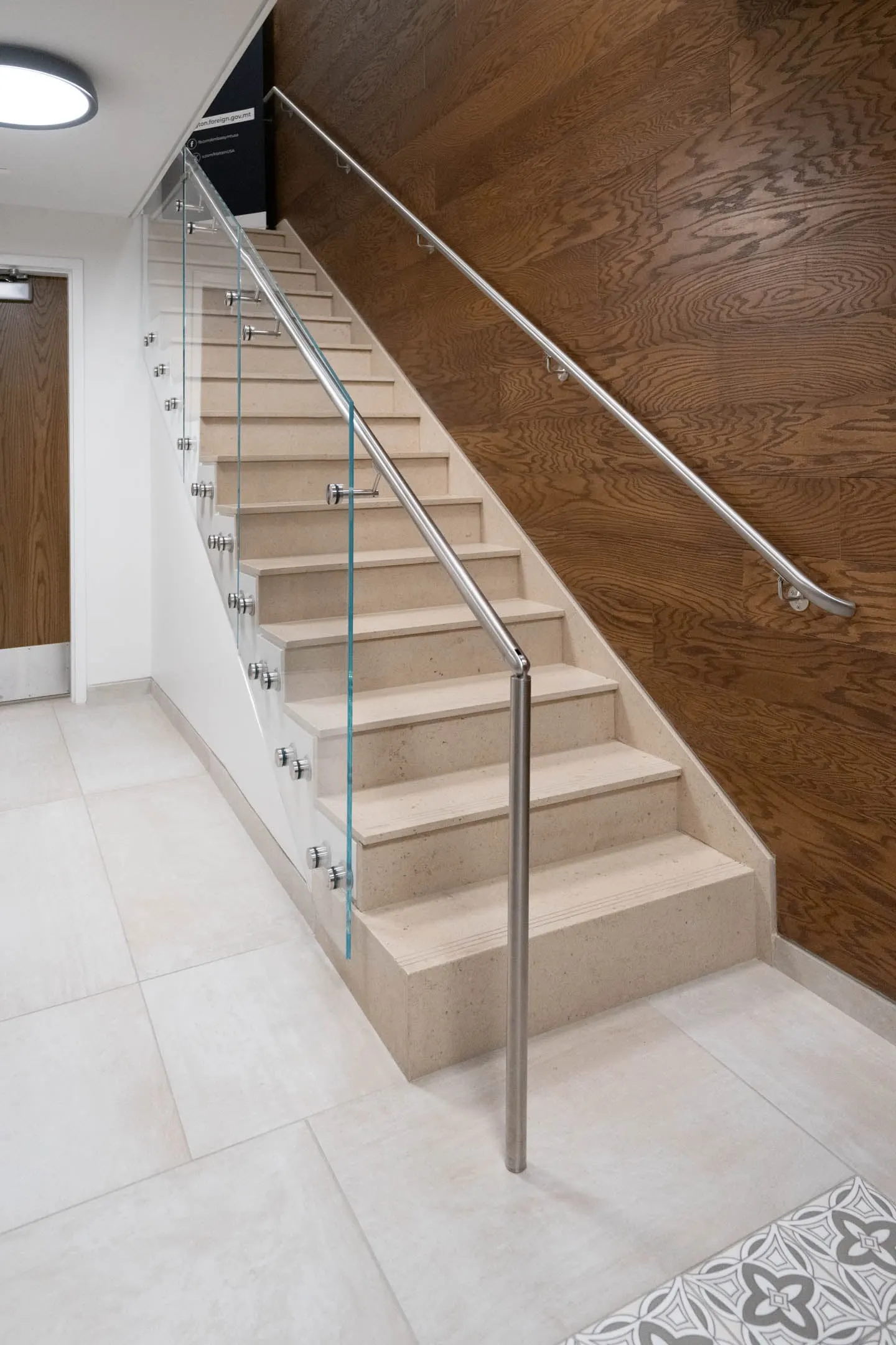Pale stone steps between a glass panel railing and a continuous round stainless handrail