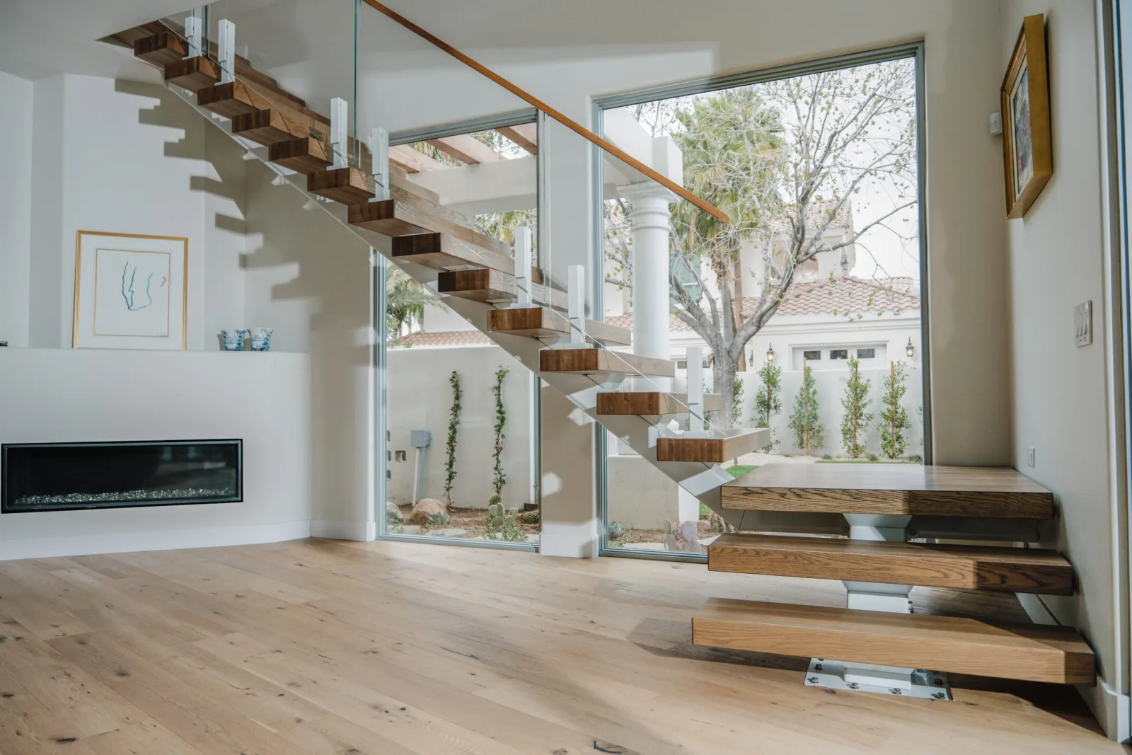 Wood treads on a white stringer with glass railing beside a courtyard window and fireplace