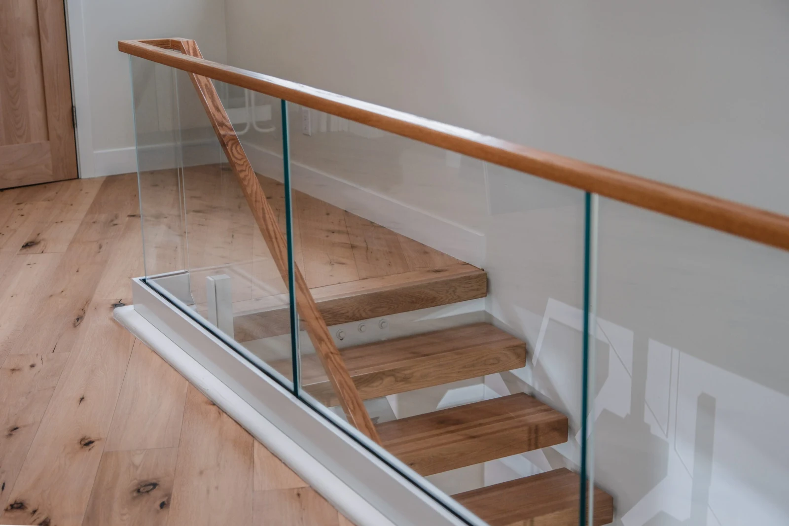Wood handrail curving above glass panels beside open wood treads