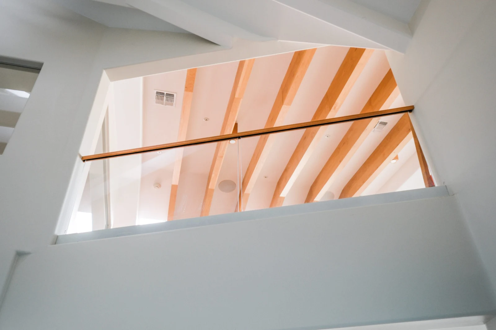Upward view of a wood handrail and glass below a beamed white ceiling