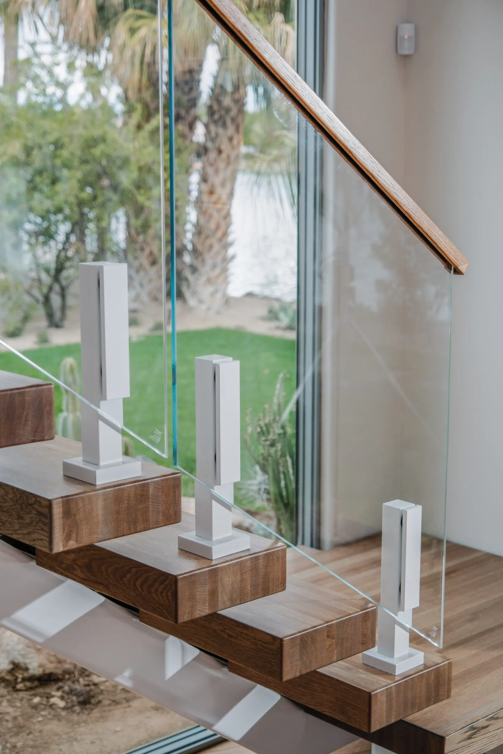 Angled view of treads, glass panels and a wood handrail toward the yard