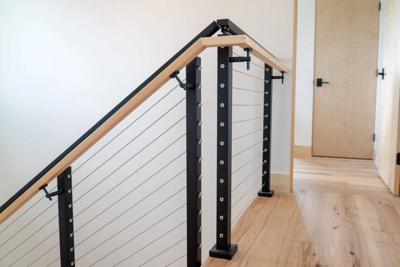Upstairs hall railing of black posts and cables capped with a wood rail