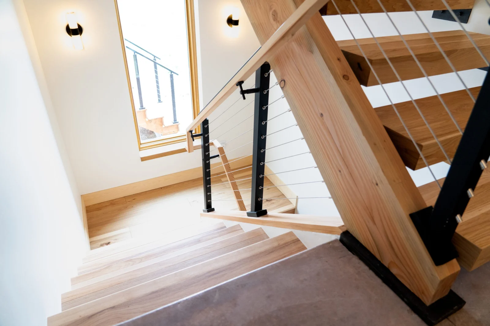 Stair descending past black posts and cables toward a window-lit landing