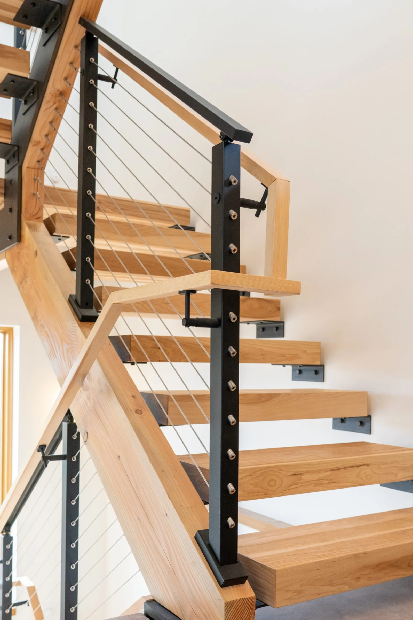 Wood treads bolted to a beam with black posts, cables, and a wood top rail