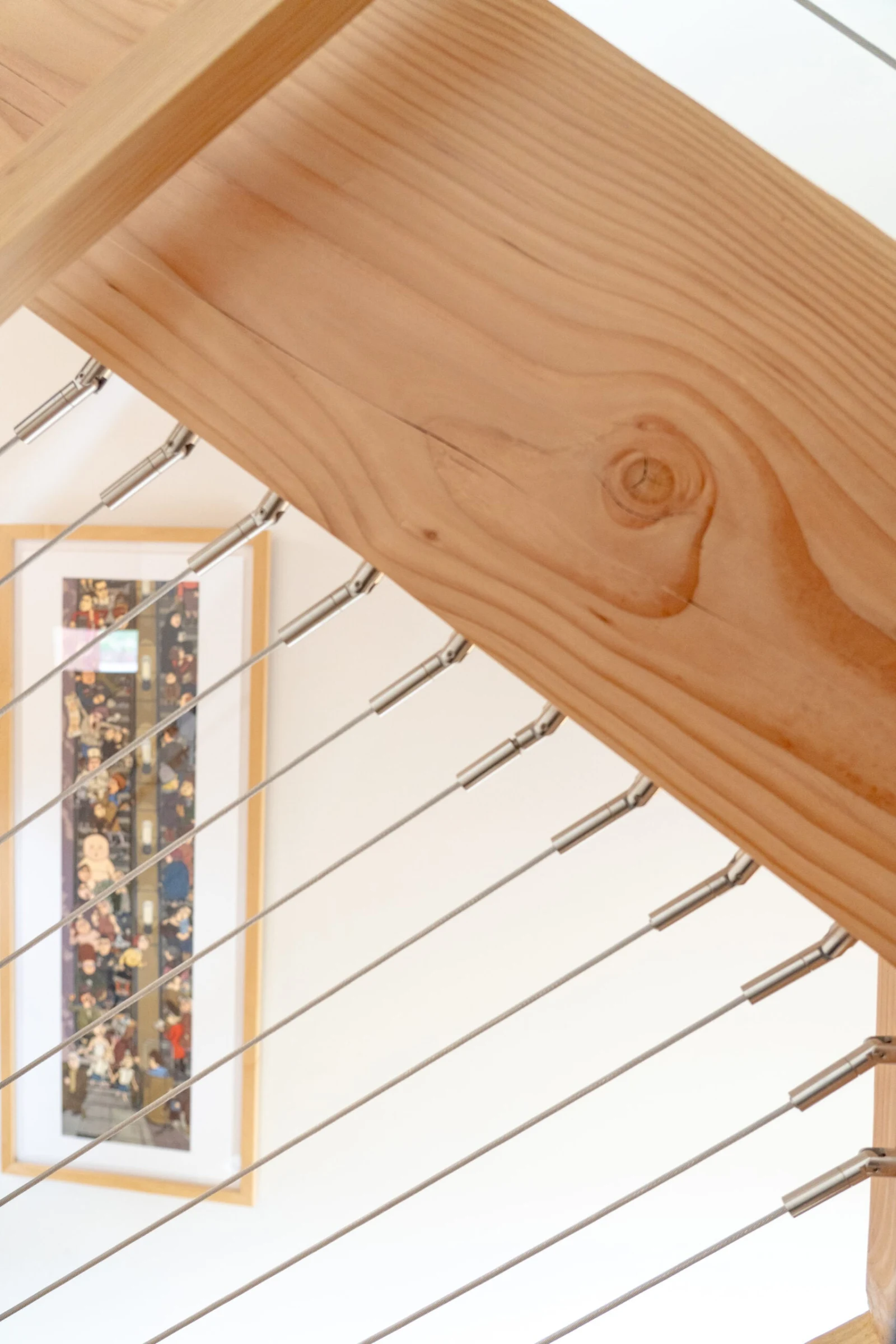 Underside of a wood handrail with cables angling toward a framed artwork