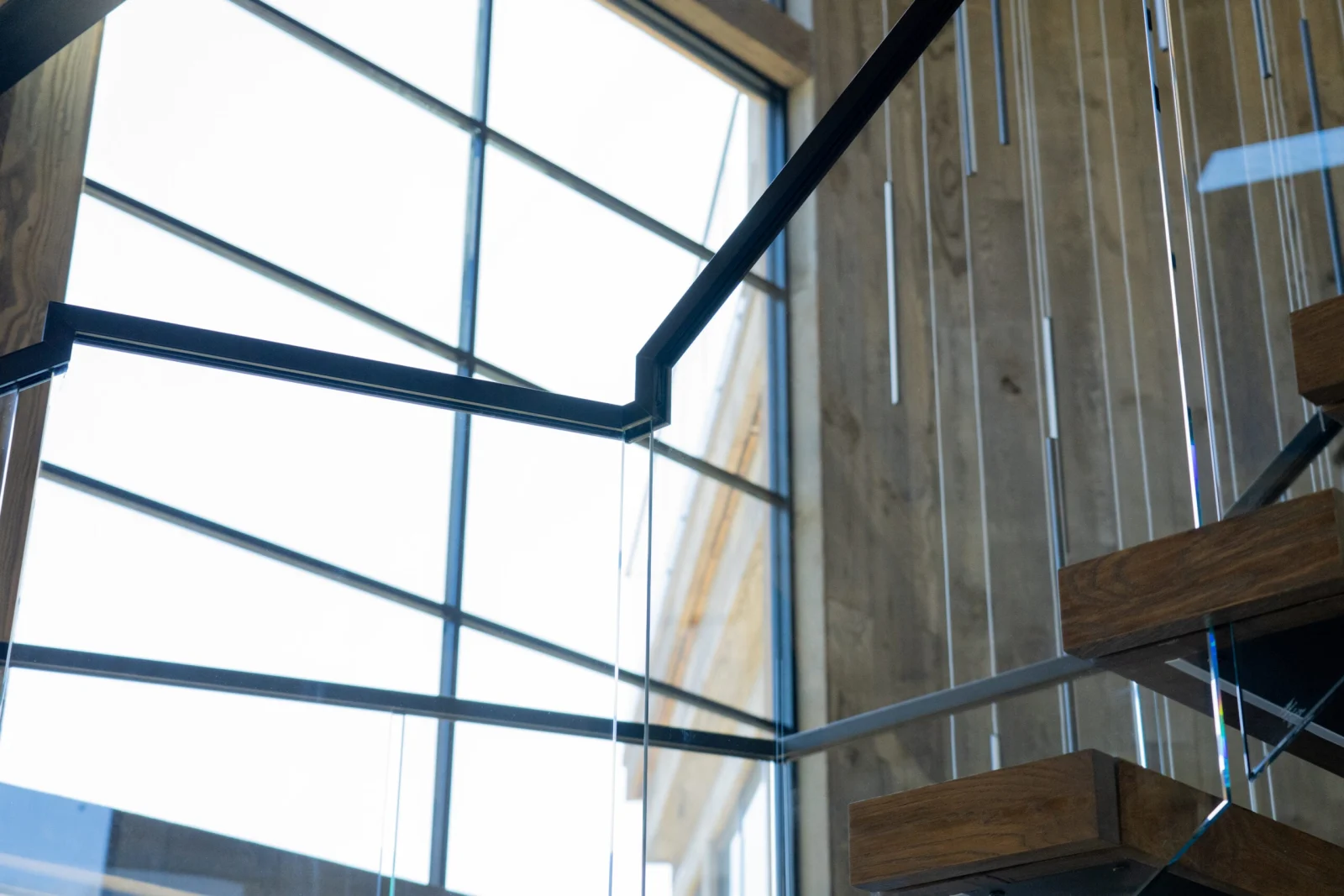 Looking up at the black handrail and glass panels against a soaring window wall