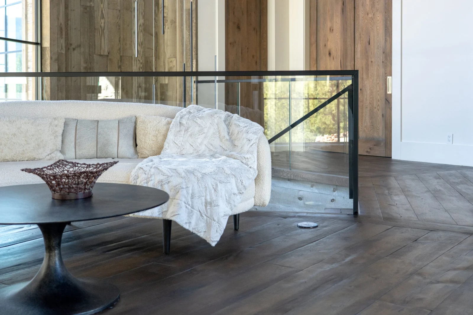Living room seating beside a balcony run of glass railing on wide plank flooring