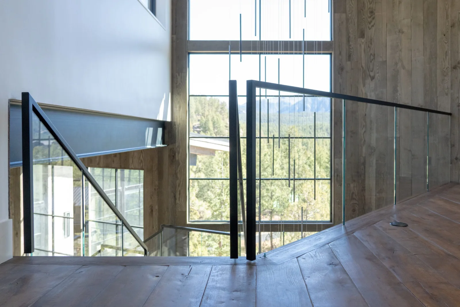 Upper landing glass railing overlooking a switchback stair and wooded valley beyond tall windows