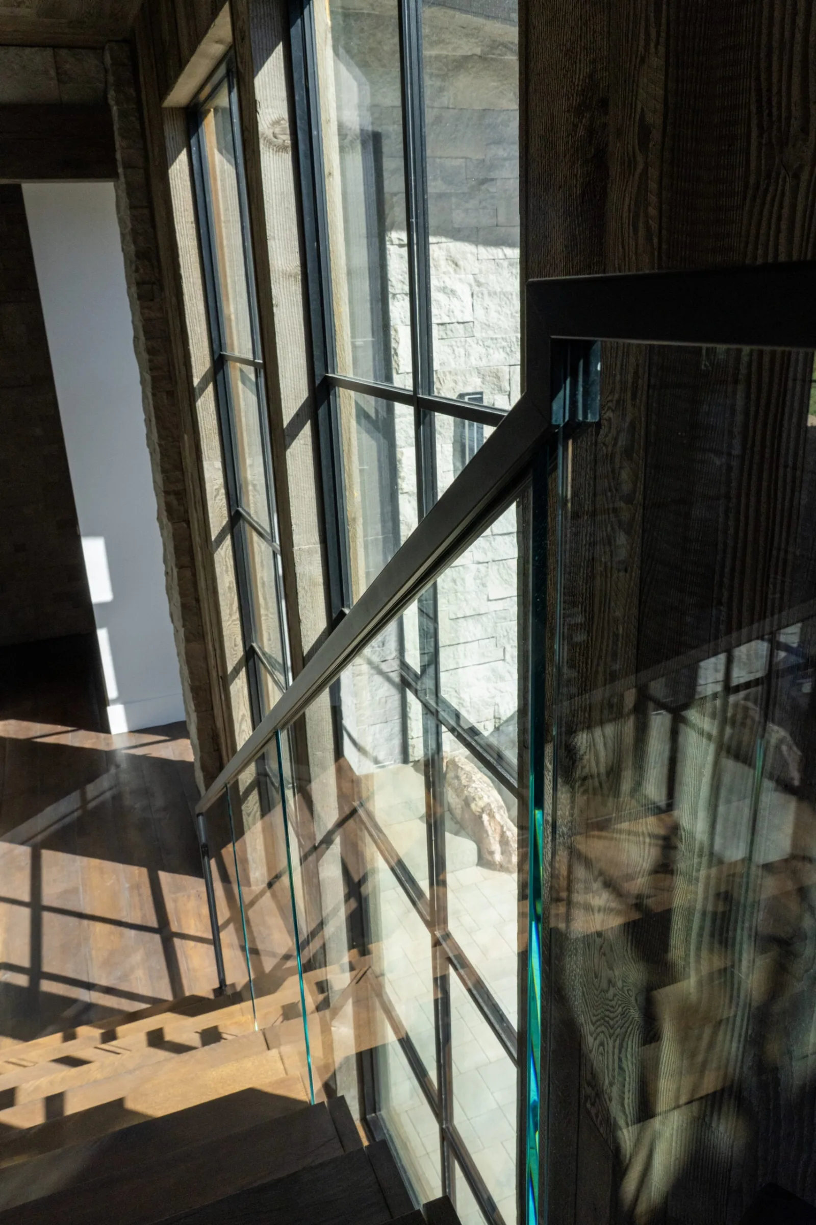 Glass railing panel and black top rail beside a tall gridded window wall