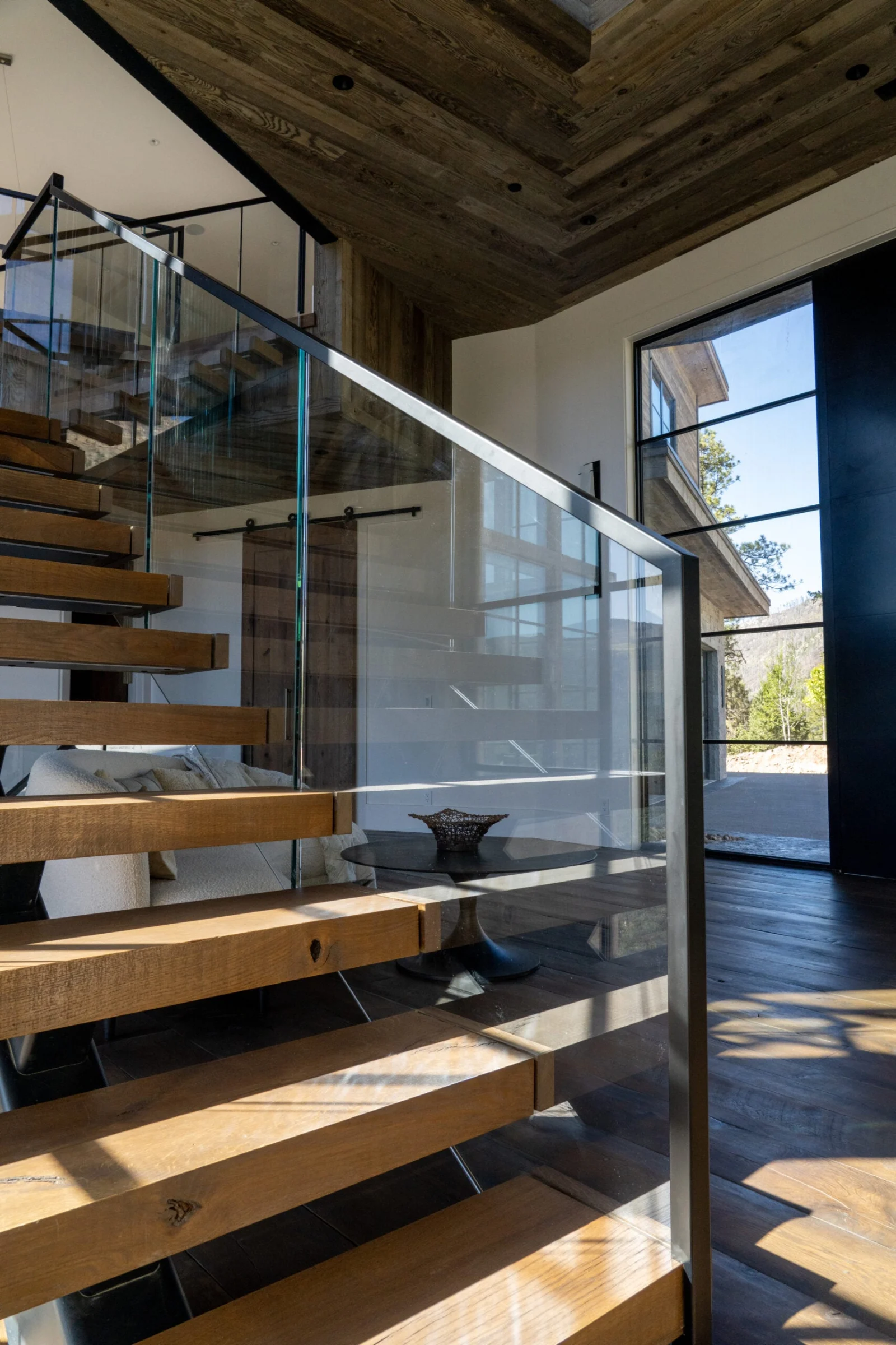 Glass railing on a floating stair with wood treads beneath a reclaimed timber ceiling