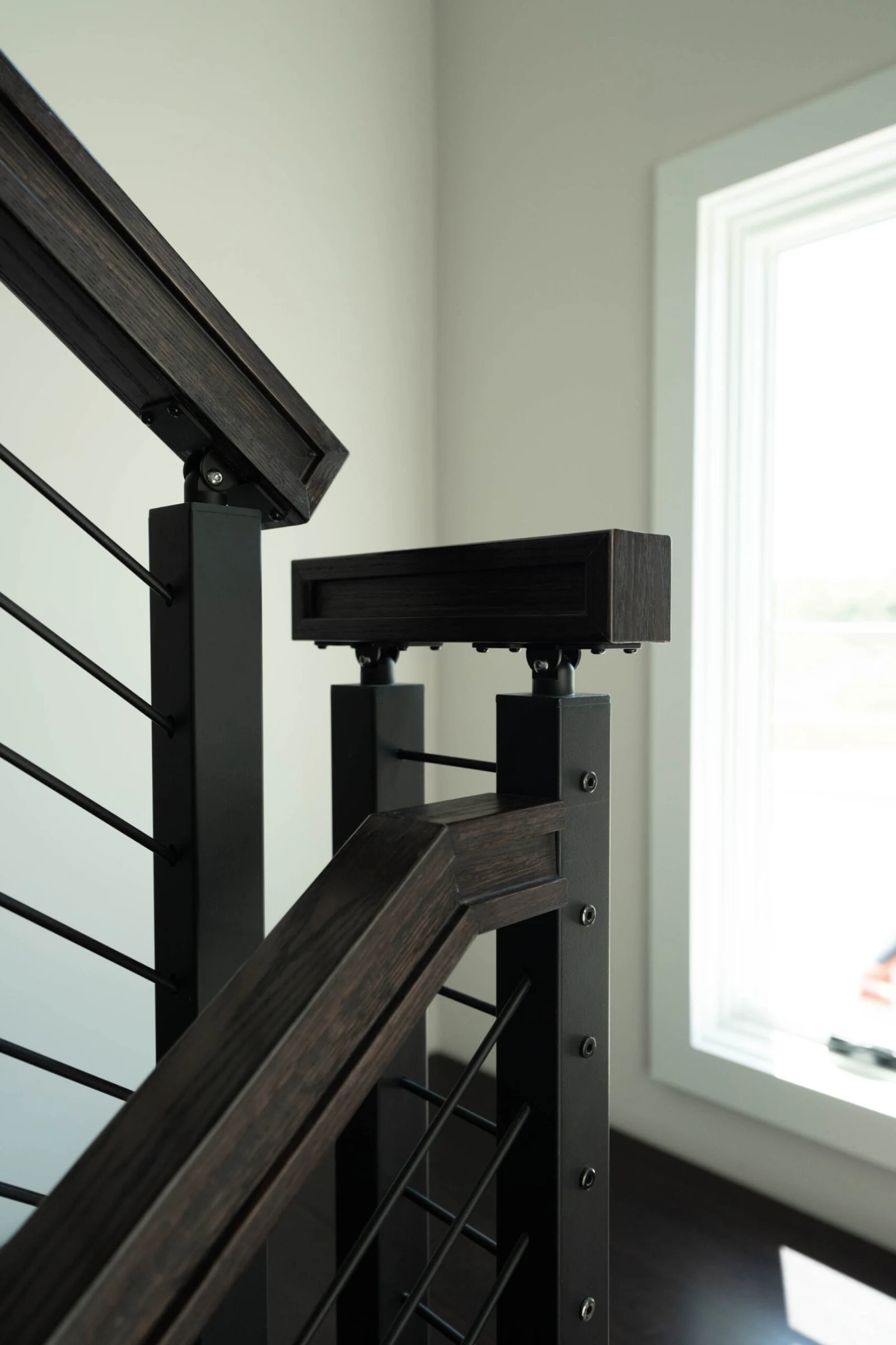 Newel post cap where the wood handrail meets rod infill near a window