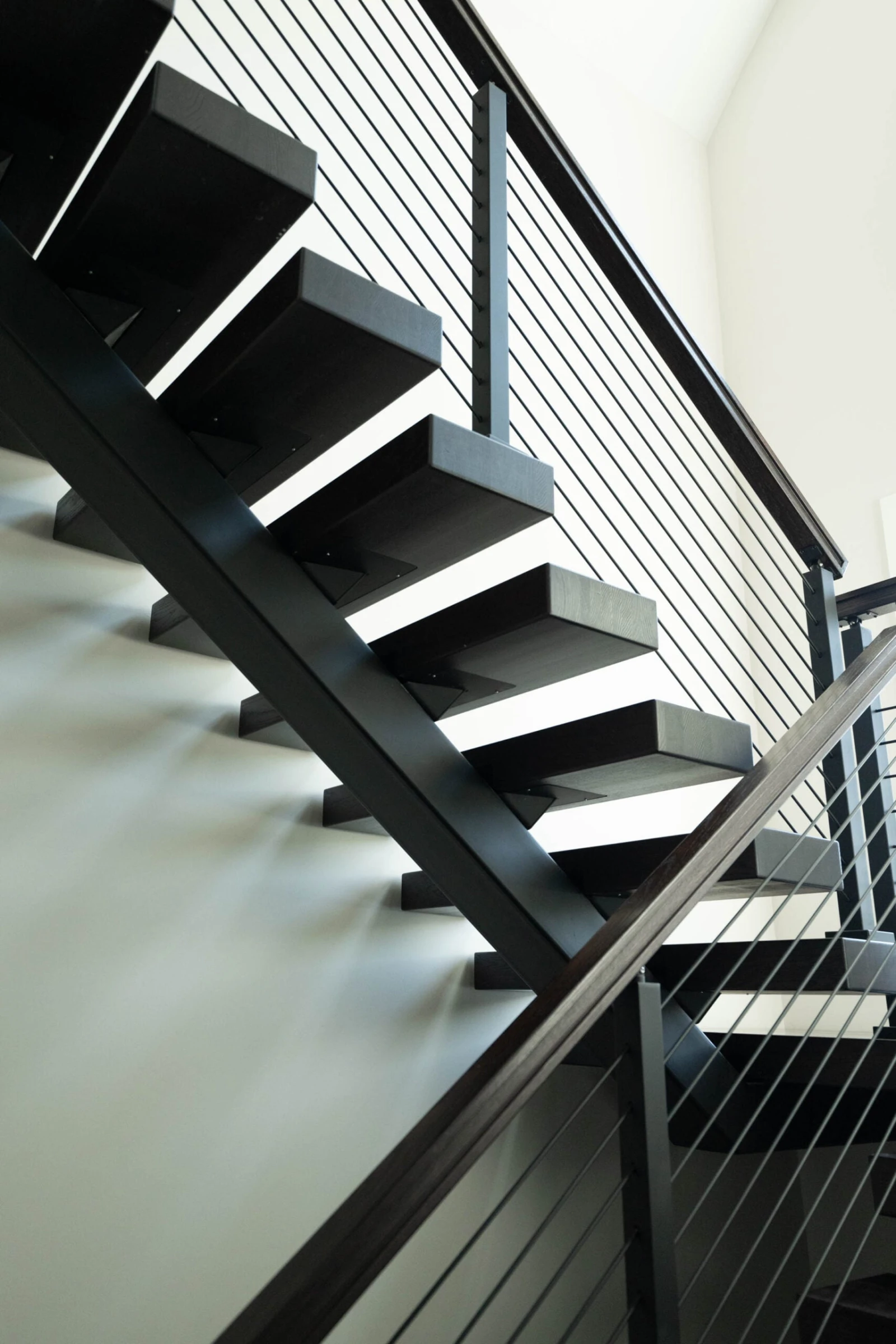 Looking up at a black center stringer stair with dark treads and rod infill