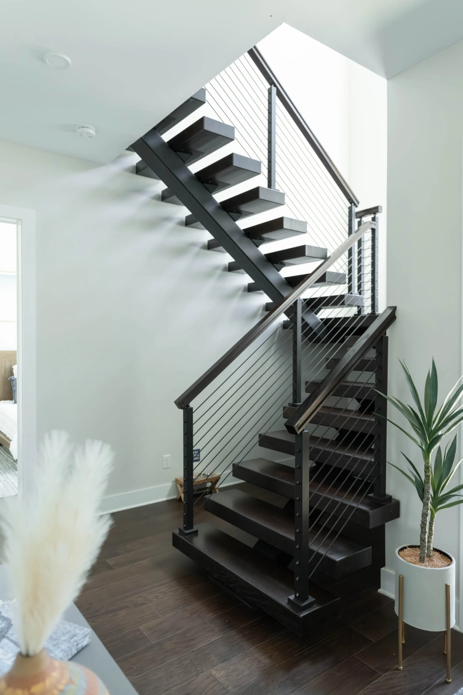 Dark stained switchback floating stair with rod railing and wood handrail in an entry