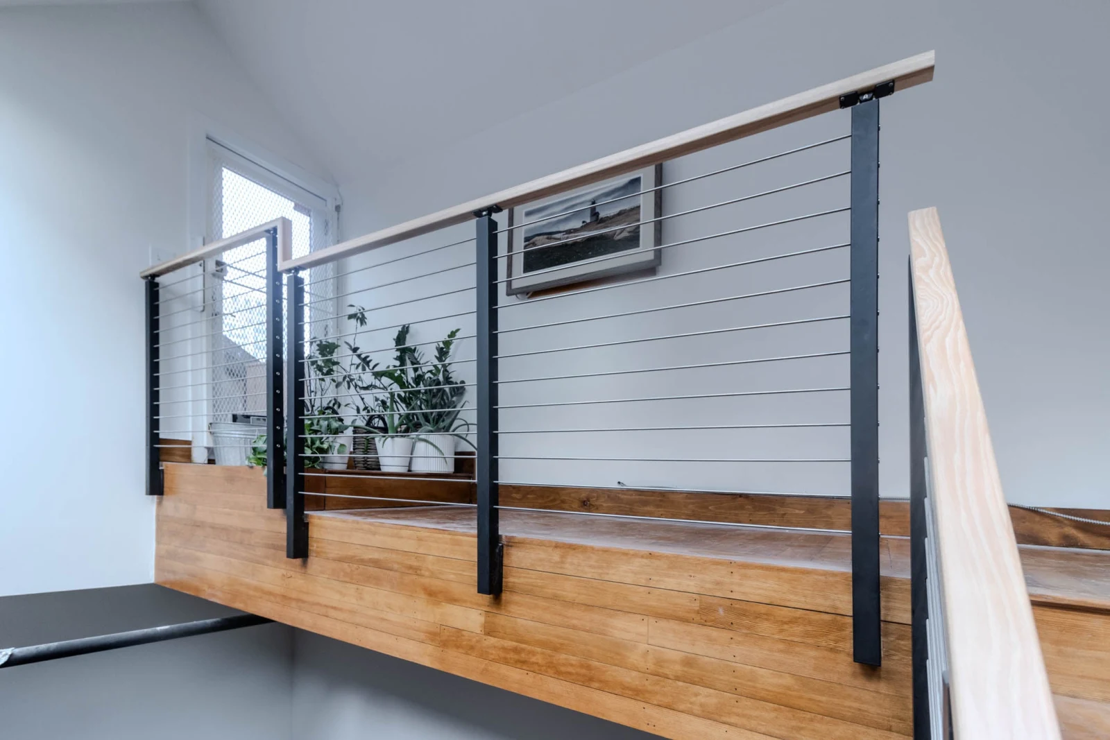 Loft-level rod railing with black posts and a light wood top rail on a shiplap wall