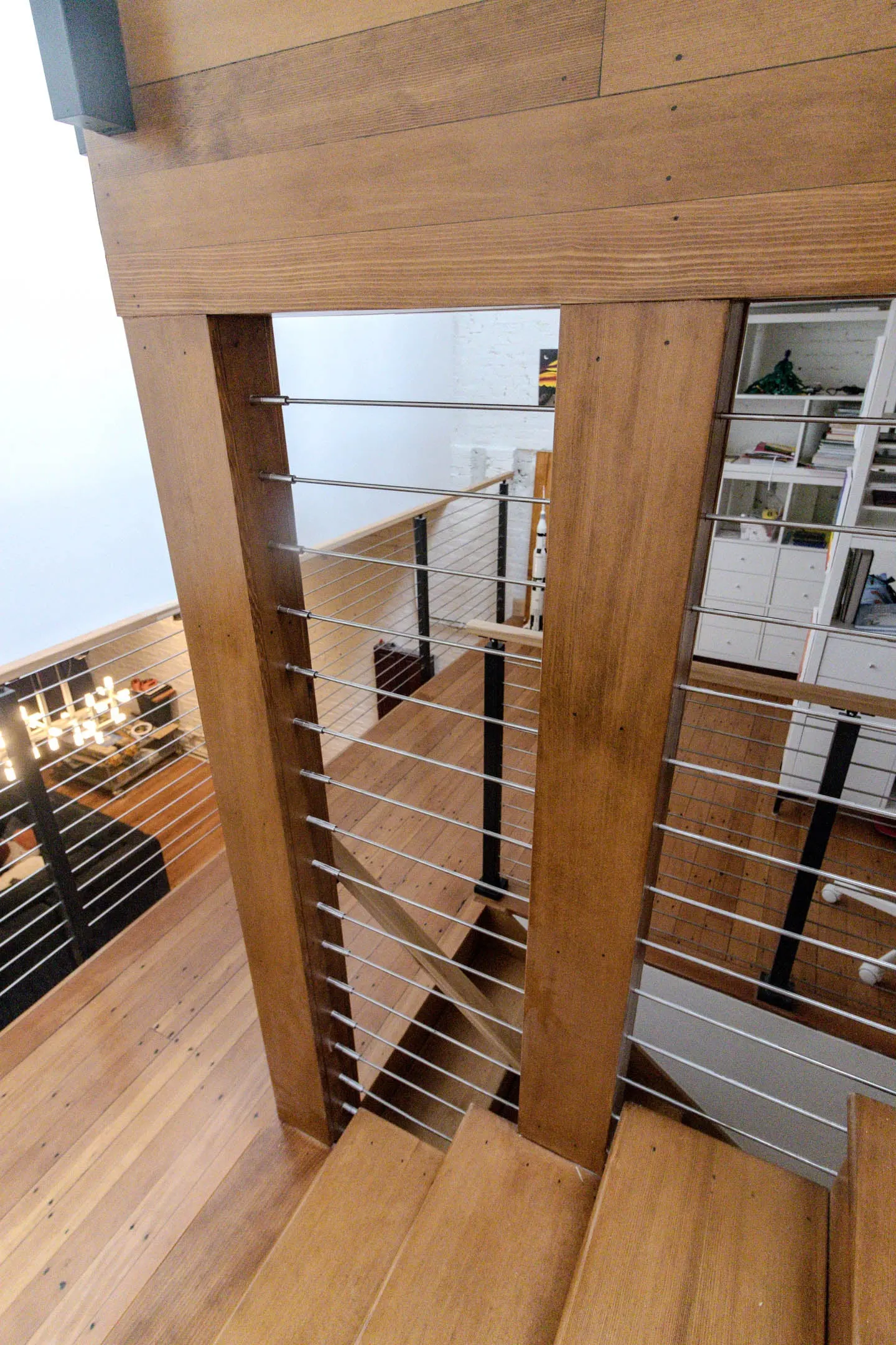 Looking down a wood-framed stairwell with rod railing panels toward the kitchen
