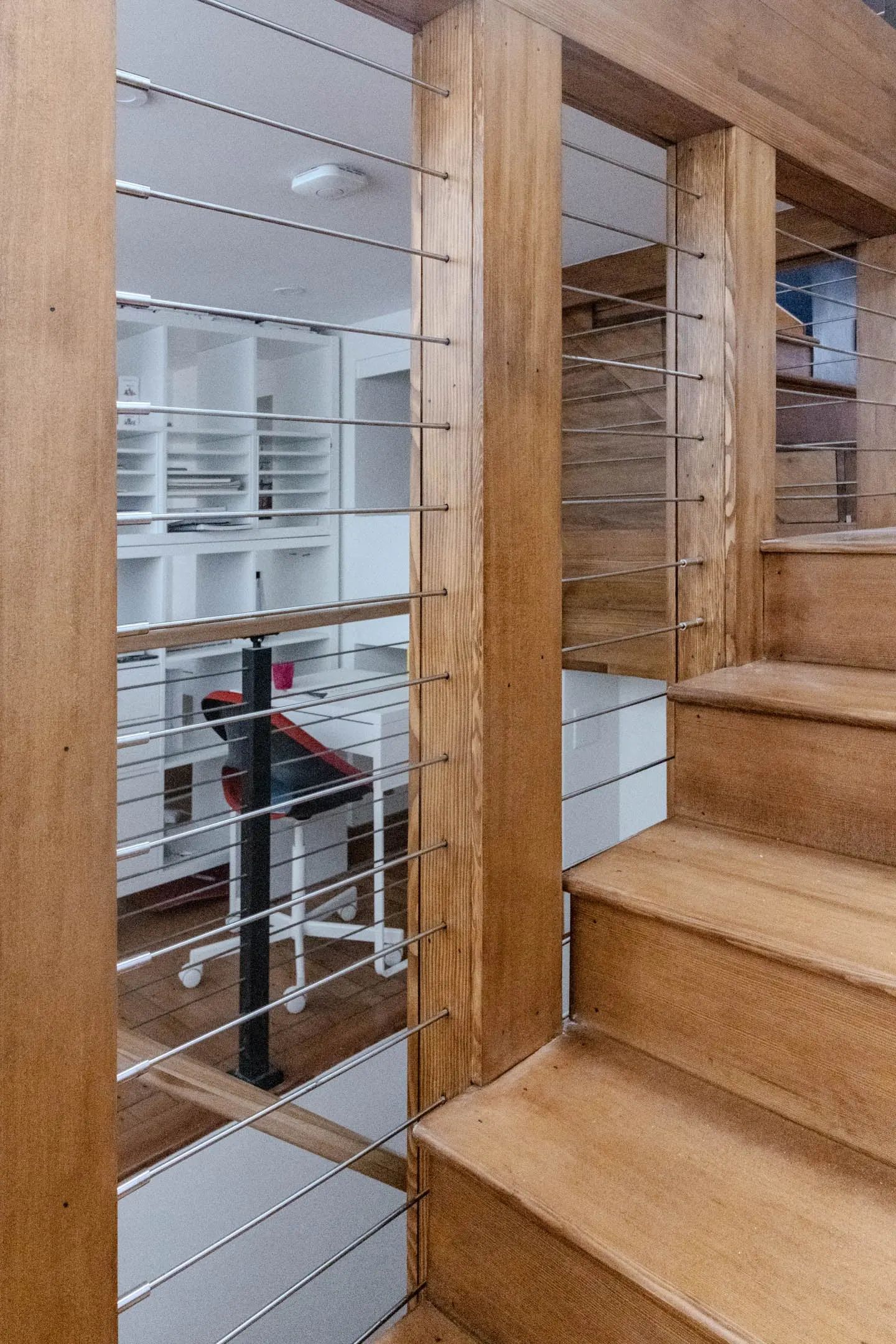 Horizontal rod infill threads through wood posts on a loft stair landing