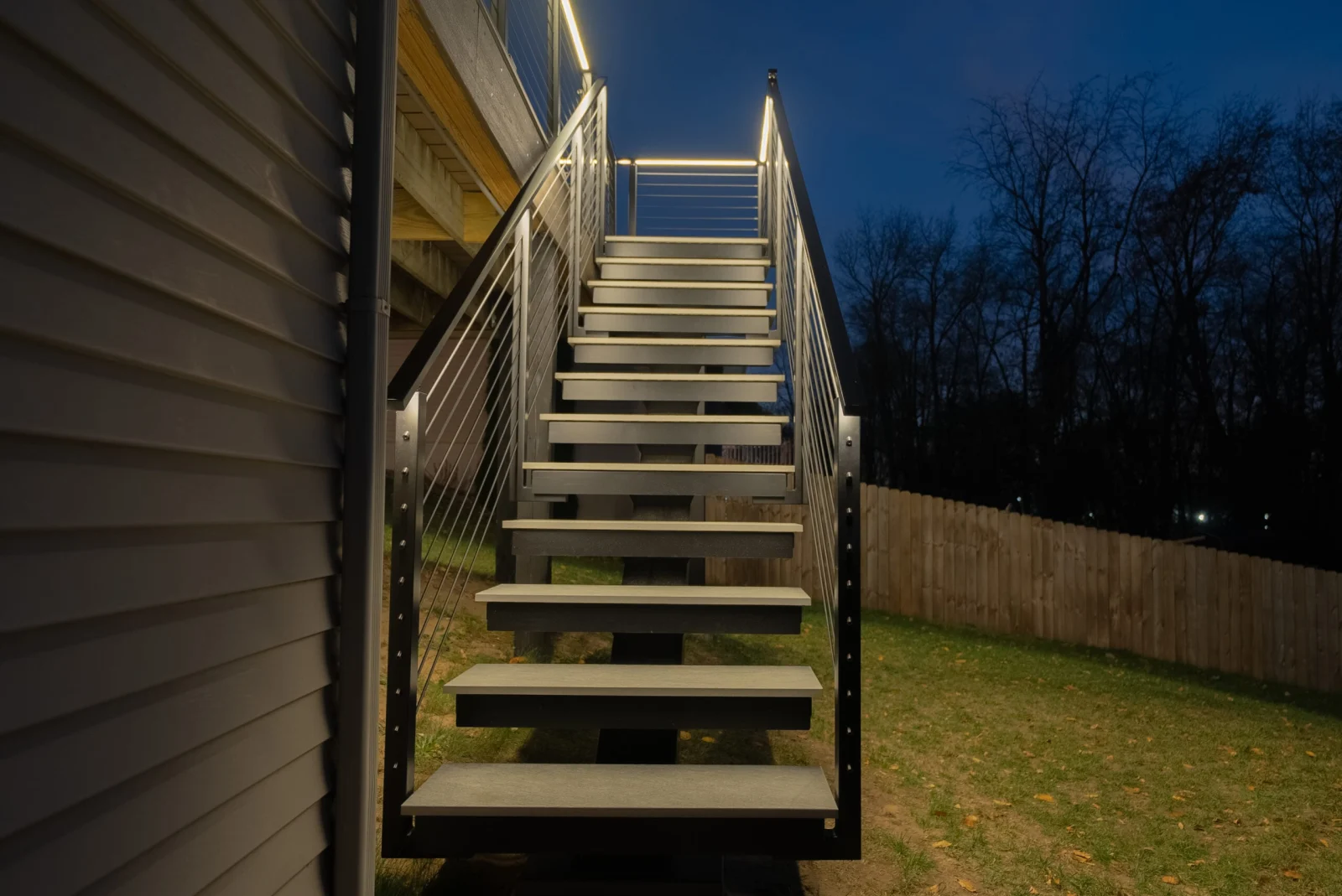 Outdoor stair climbing to a deck at dusk, LED handrail glowing over gray treads