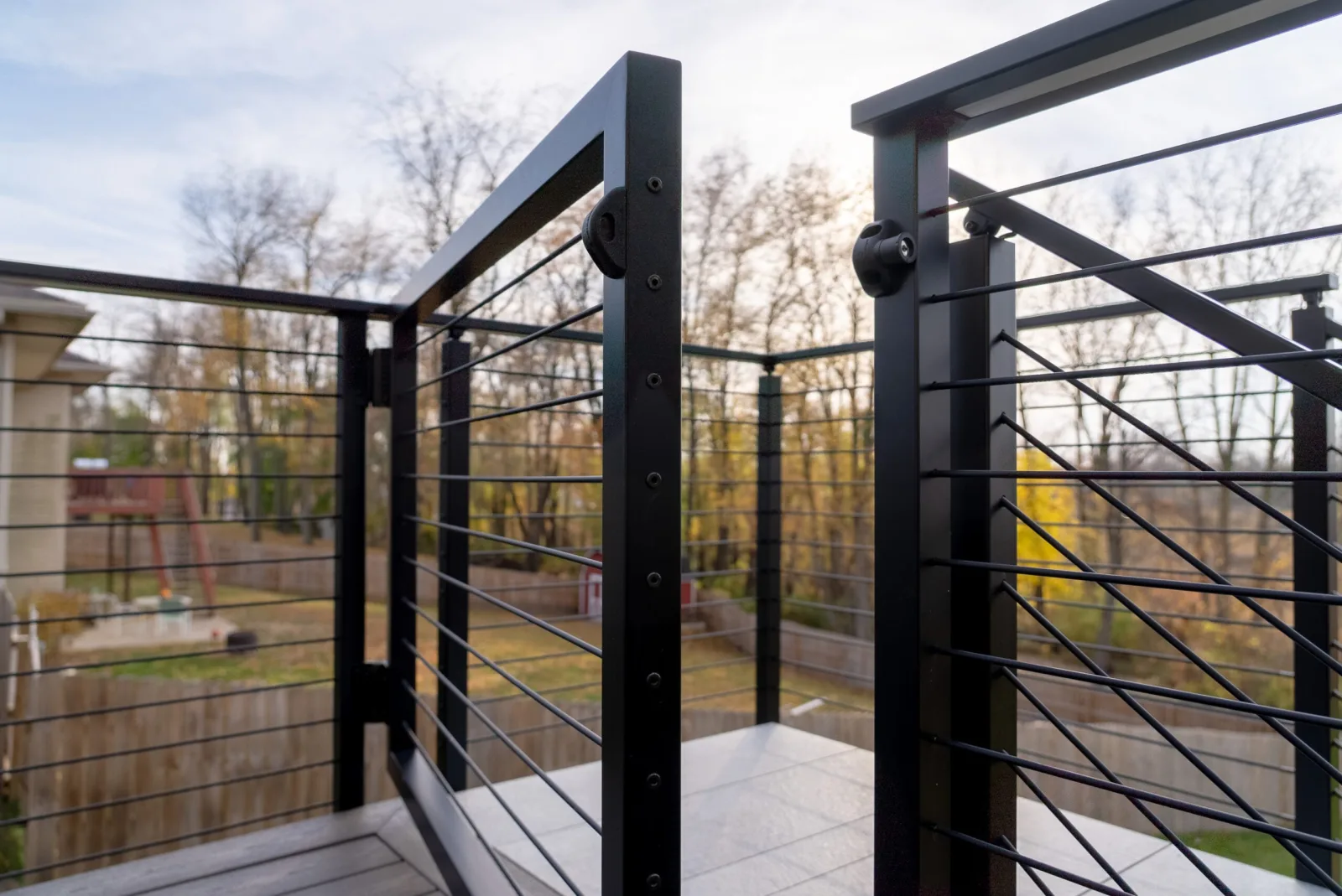 Black rod railing turning a deck corner above a fenced yard and bare trees