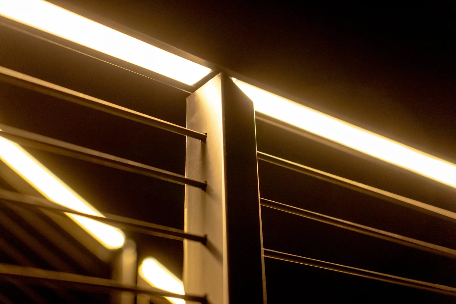 Illuminated top rail glowing along black posts and rods at night