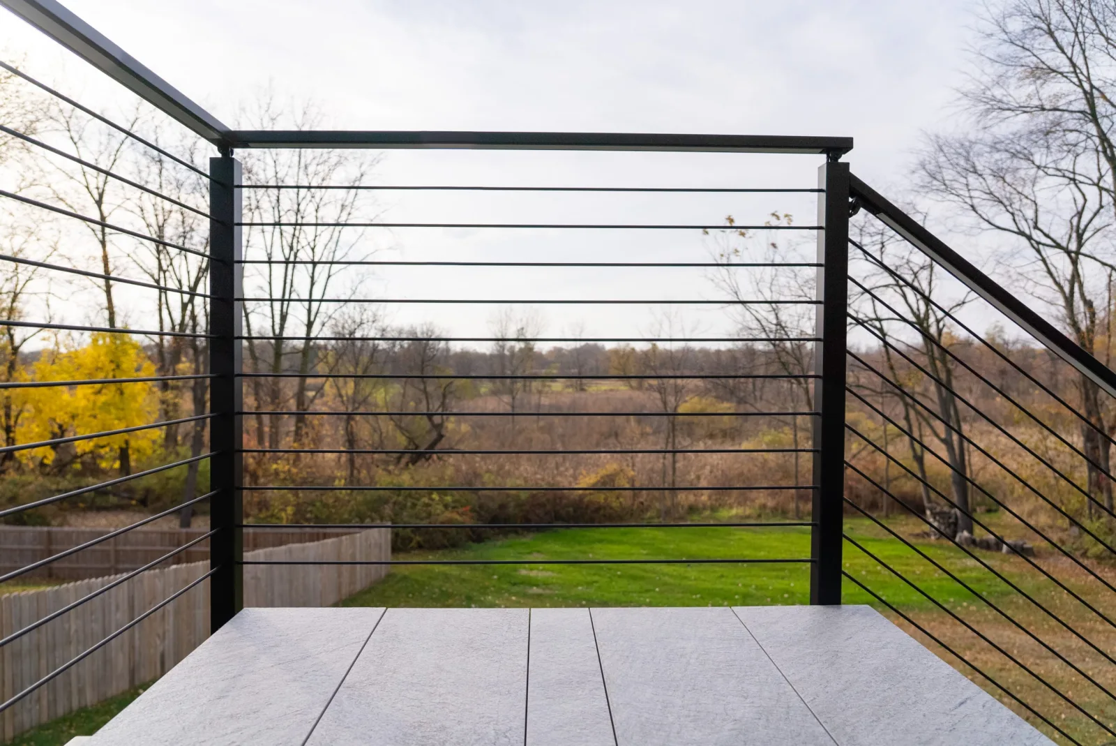 Deck landing looking out over rod railing toward a field and open sky